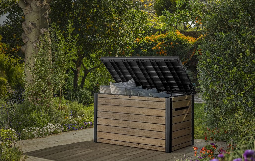Eine hölzerne Gartenbox mit geöffnetem Deckel steht auf einer Holzterrasse im Garten, gefüllt mit Kissen.