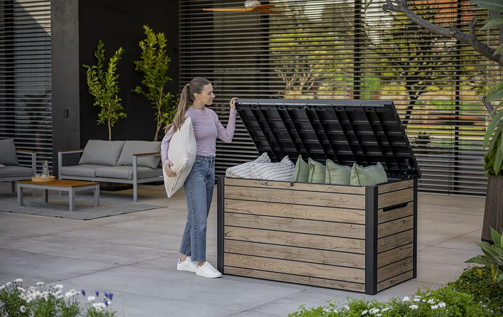 Eine Frau hält ein Kissen neben einer geöffneten Outdoor-Kissenbox auf einer Terrasse.