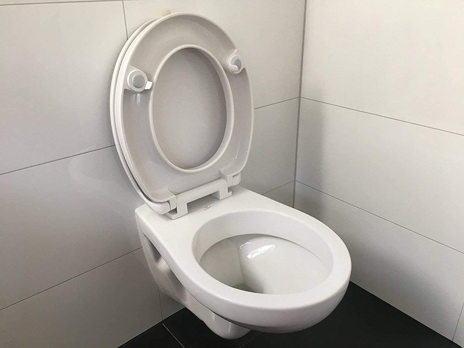 Un water bianco con il coperchio aperto contro una parete di piastrelle bianche.