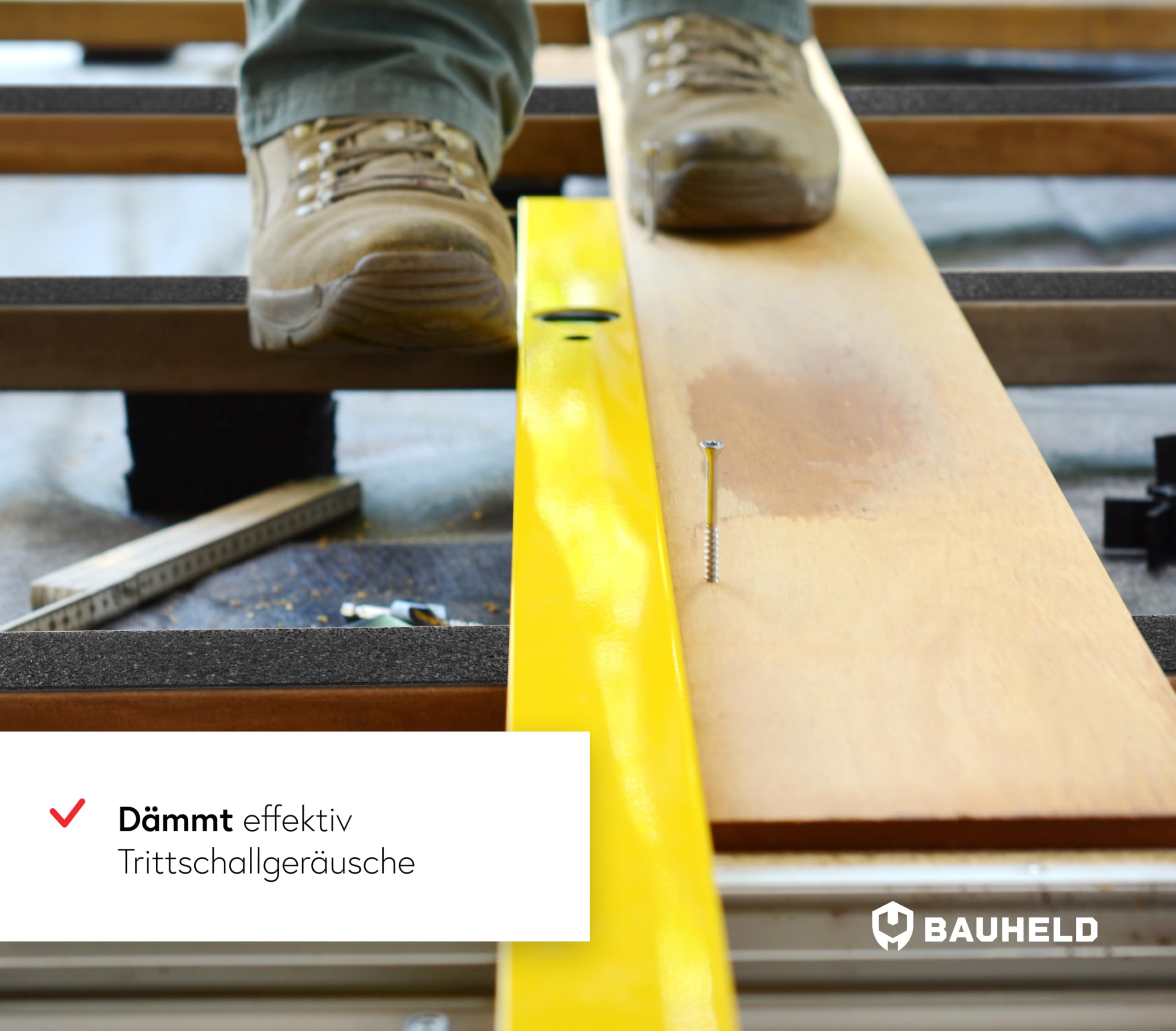 Jambes d'ouvrier sur des planches en bois près d'un niveau jaune et d'une vis.