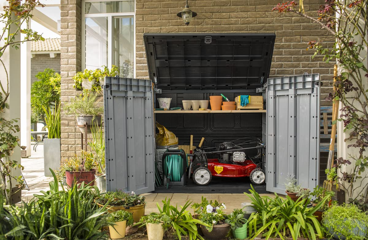 Ein grauer Gartenschrank mit offenem Deckel und Türen steht auf einer Terrasse, gefüllt mit Gartengeräten und Blumentöpfen.