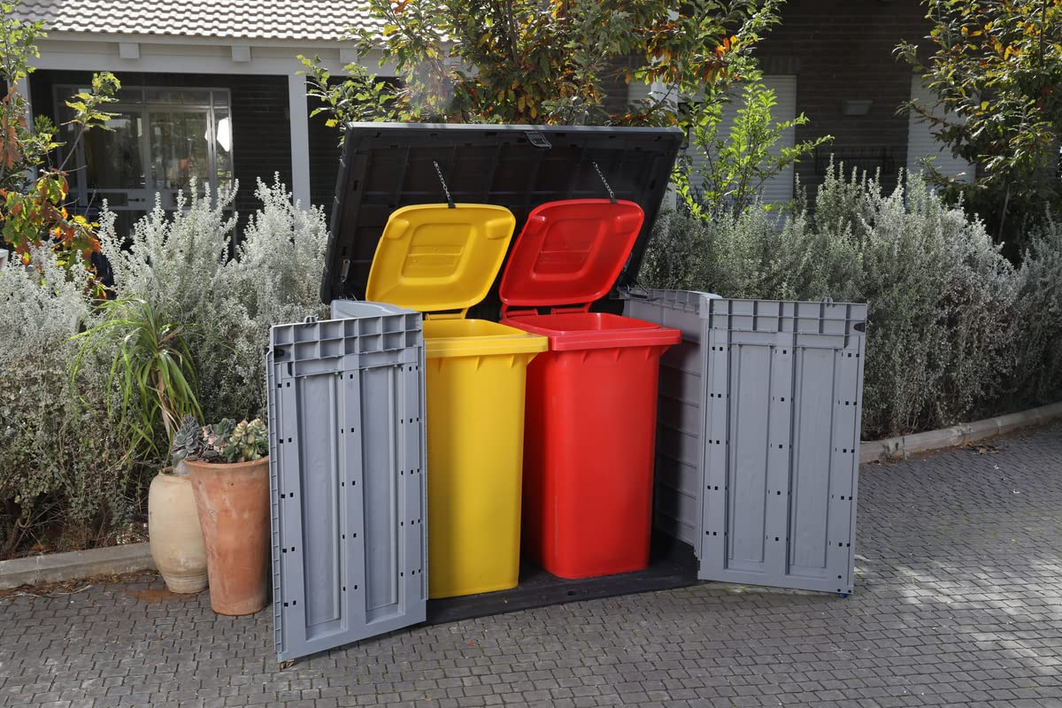 Eine offene graue Müllbox mit gelben und roten Tonnen davor.