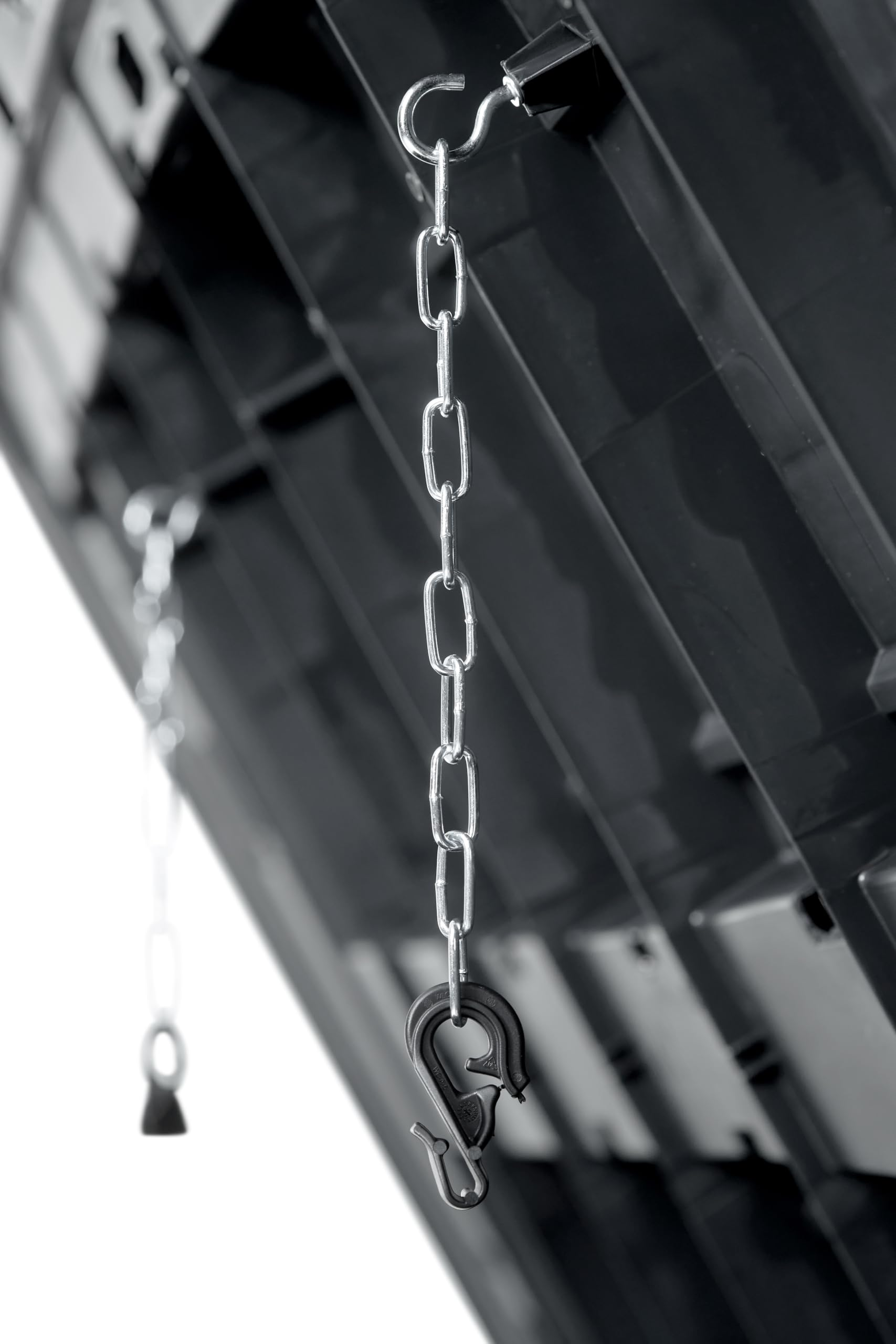 Eine Metallkette mit schwarzem Haken hängt senkrecht vor schwarzem Kunststoff.