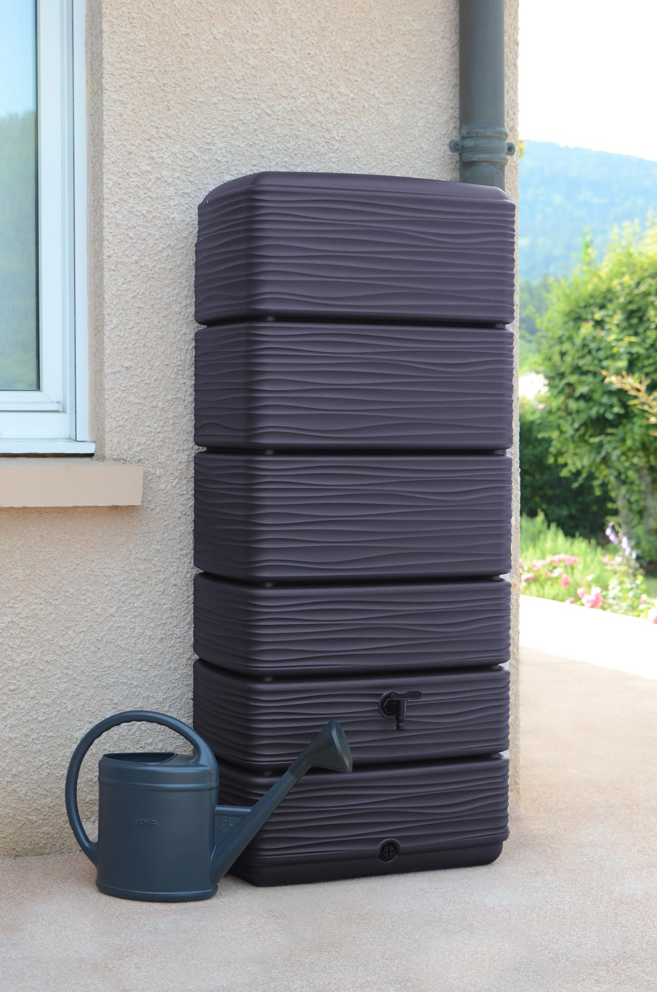 Recuperateur d eau marron fonce texture ondulee et arrosoir pose contre un mur.