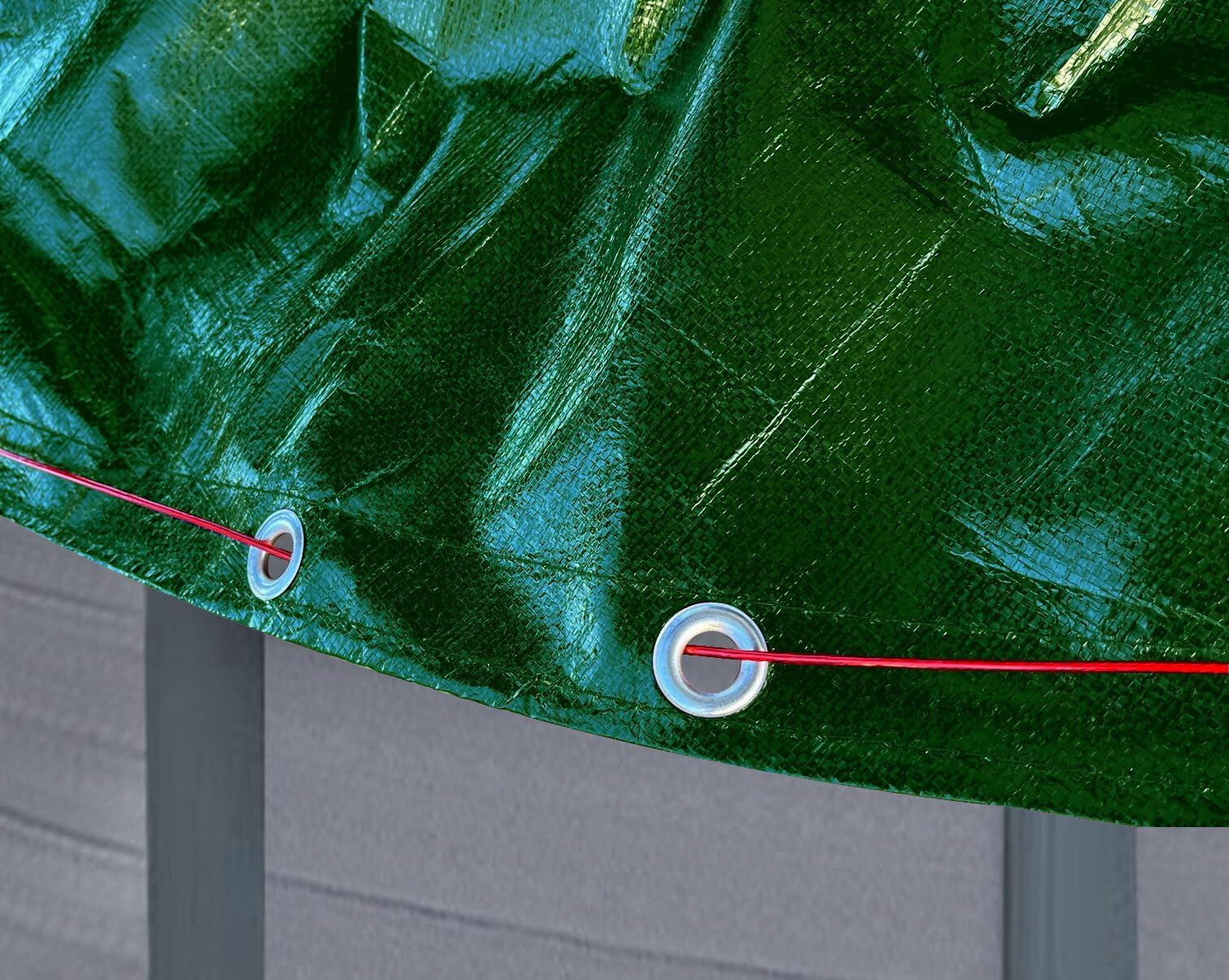 Une bâche en plastique vert brillant avec des œillets métalliques est fixée par une ficelle rouge sur fond gris.