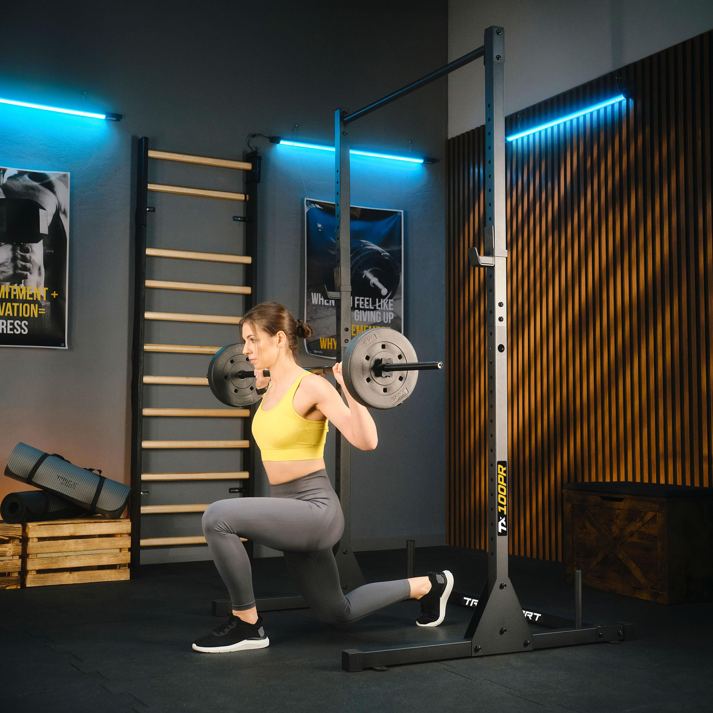 Eine Frau in Sportkleidung macht Ausfallschritte mit einer Langhantel in einem modernen Fitnessstudio.