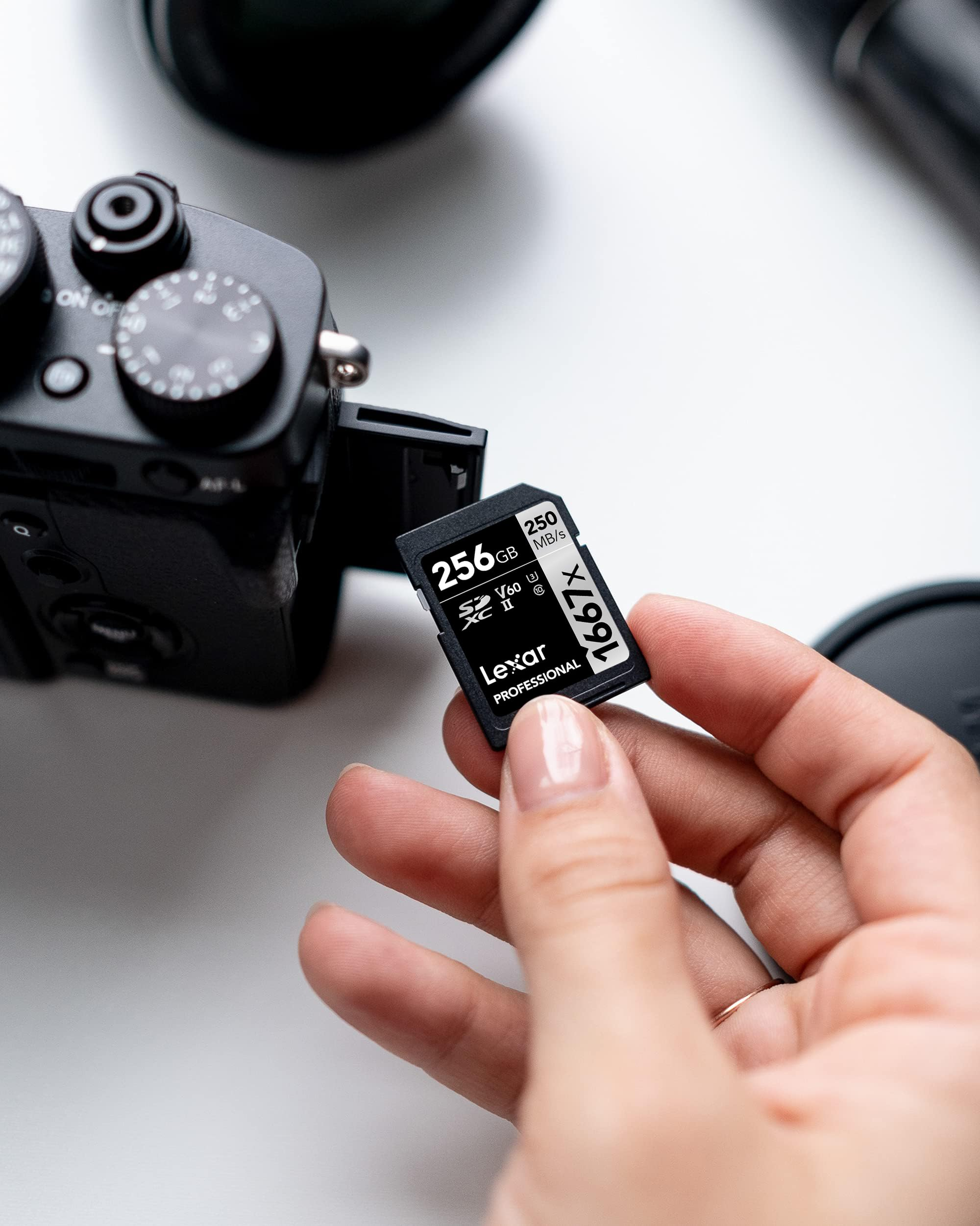 Une main tient une carte mémoire SD Lexar de 256 Go devant un appareil photo noir sur une table blanche.