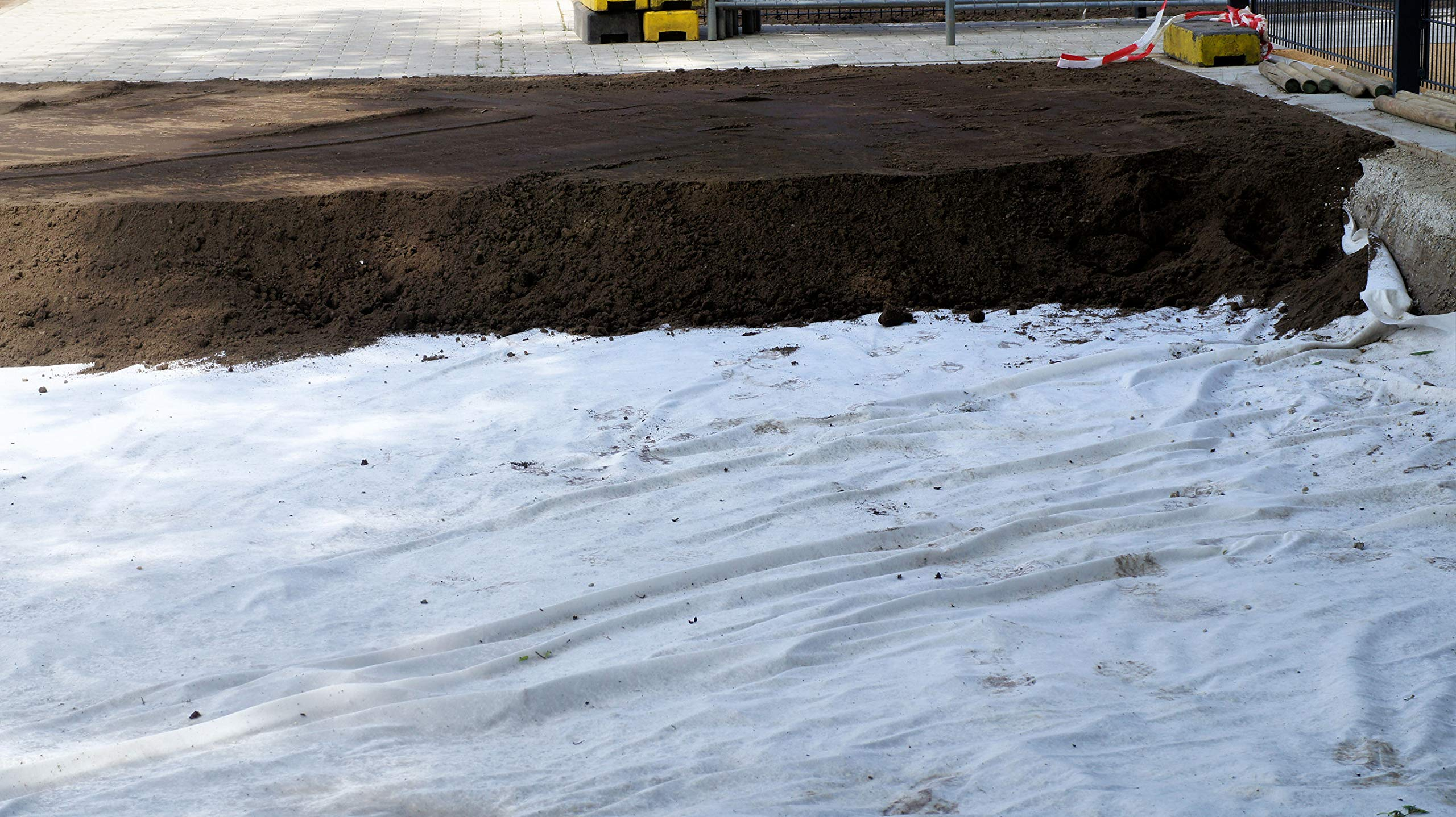 Une épaisse couche de terre repose sur un géotextile blanc sur un chantier.