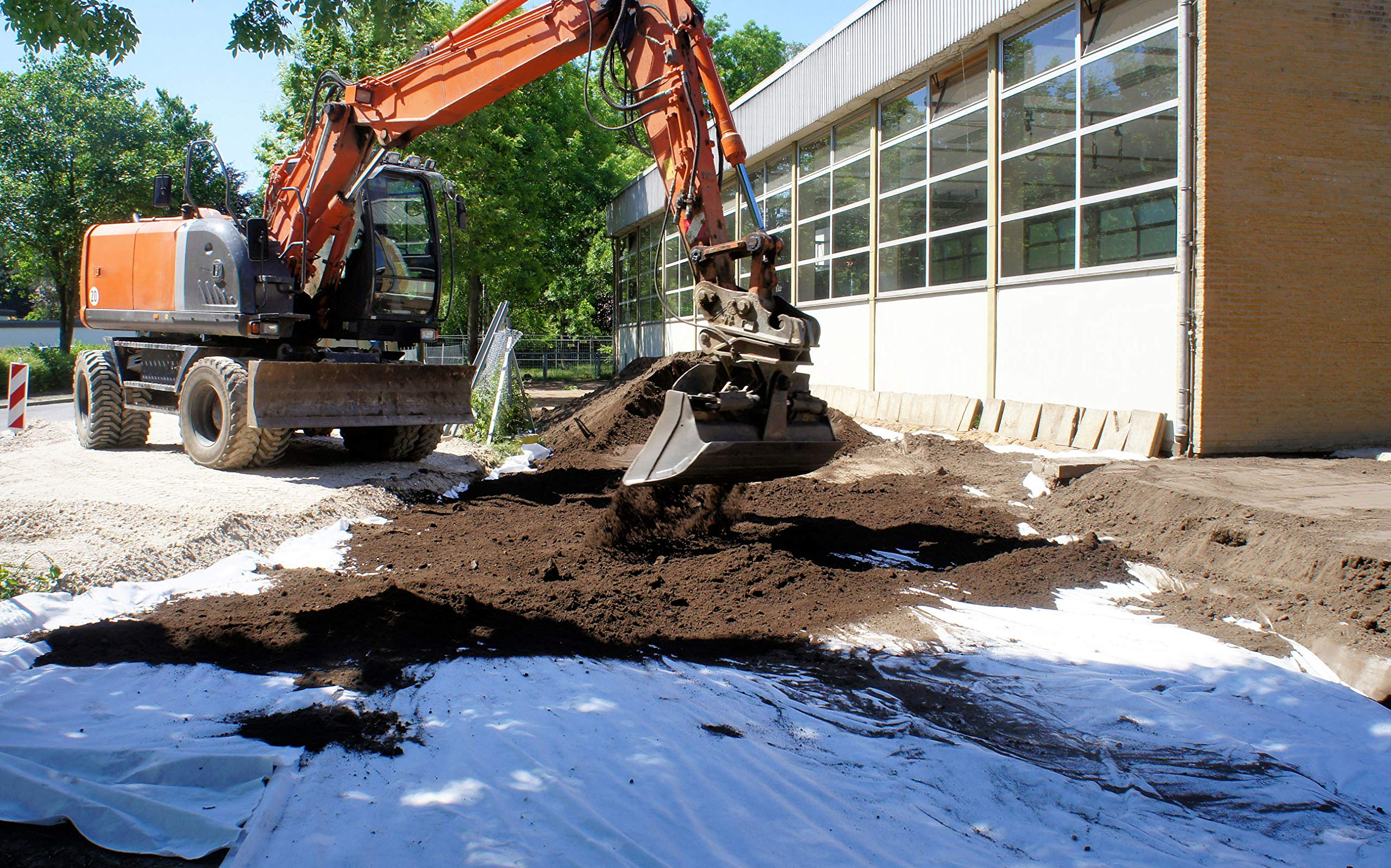 Une excavatrice orange creuse de la terre sur un chantier devant un bâtiment.
