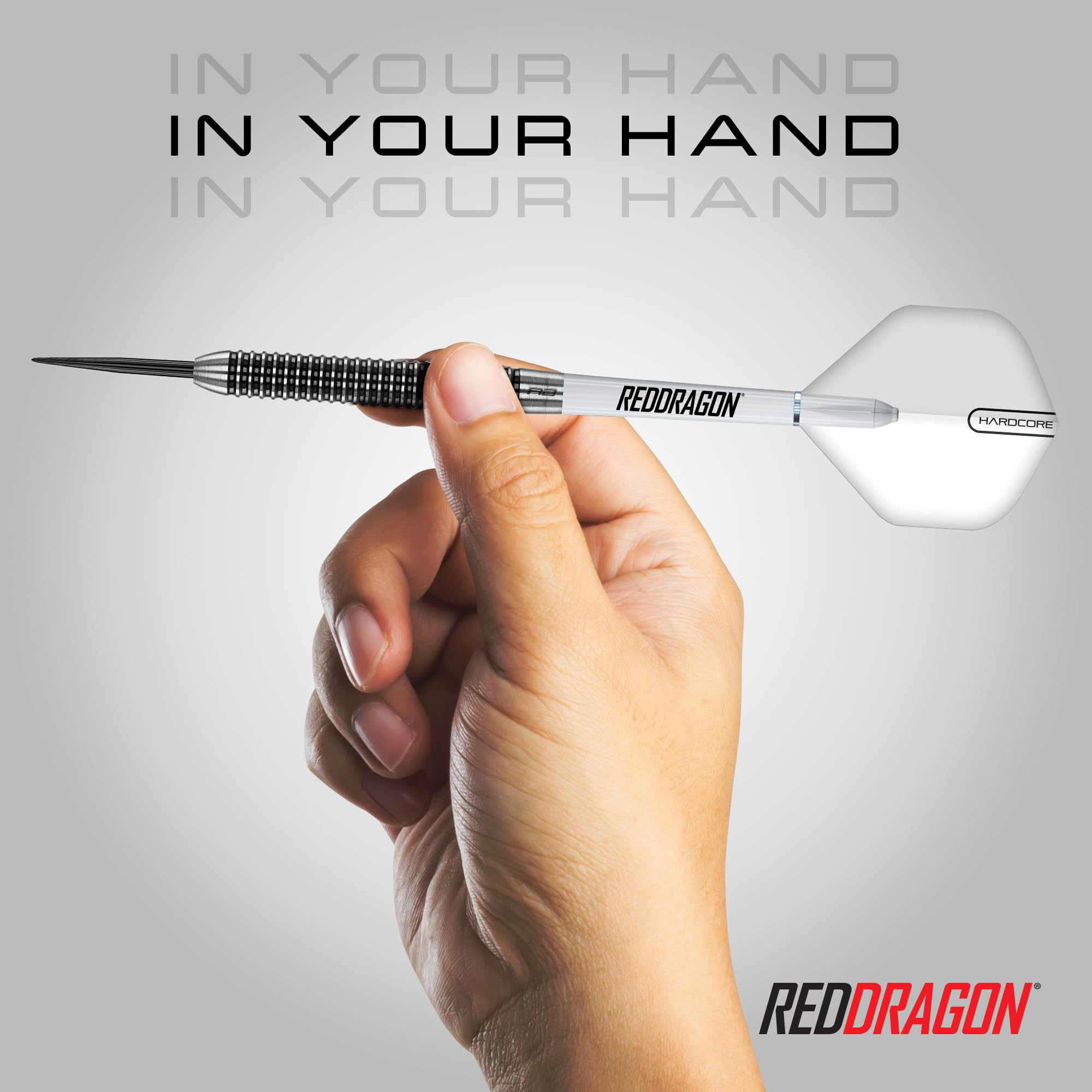 Eine Hand hält einen silbernen Red Dragon Dartpfeil vor grauem Hintergrund mit dem Text "IN YOUR HAND".