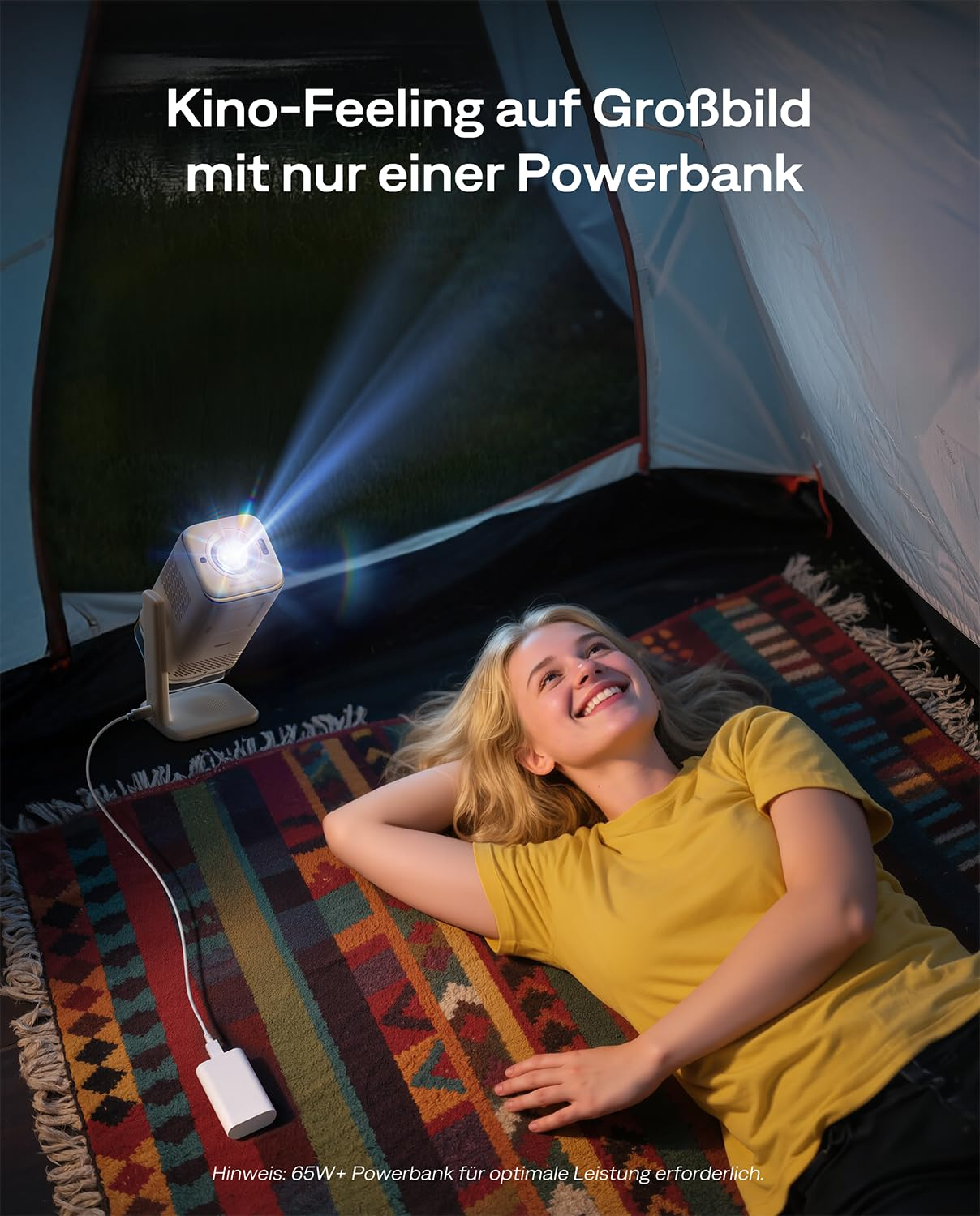 Una donna è sdraiata in tenda e guarda un proiettore collegato a un power bank.
