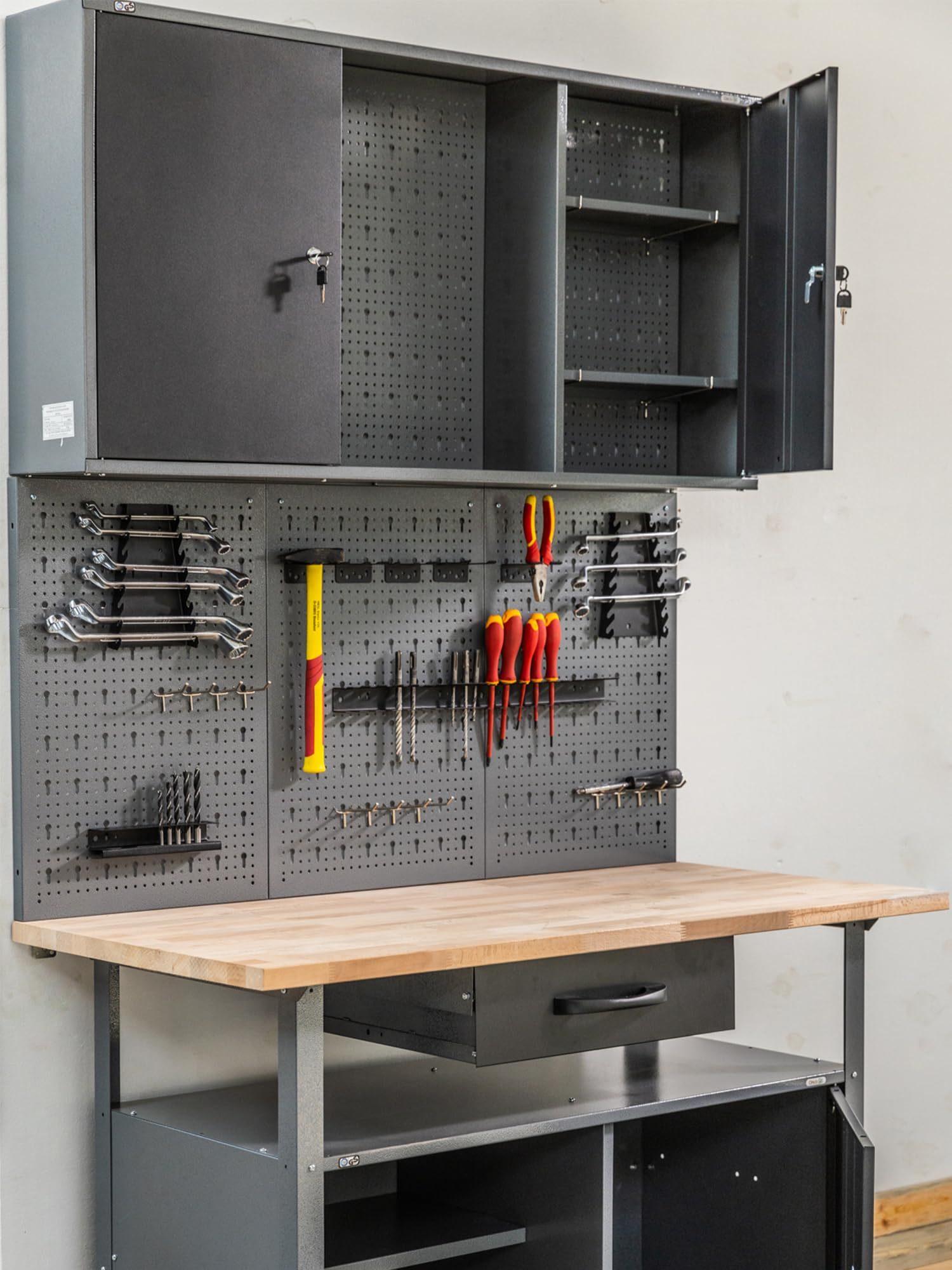 Eine Werkbank aus Holz mit einem grauen Metall-Hängeschrank und Lochwänden voller Werkzeuge wie Schraubenschlüssel und Hämmer.