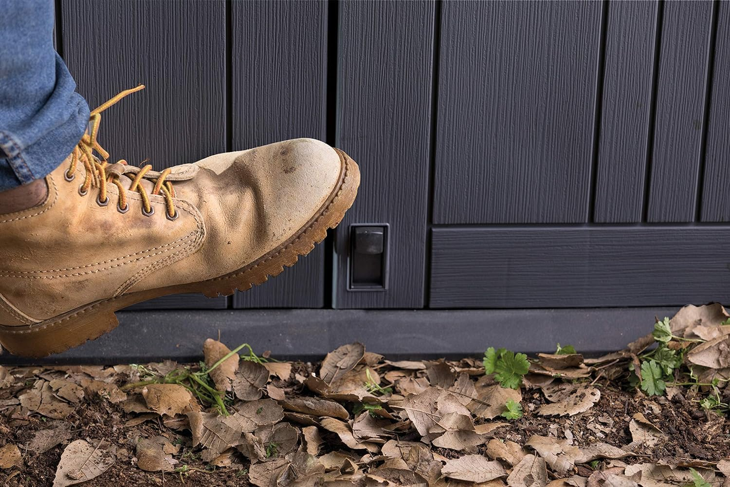 Une botte donne un coup de pied dans la porte d'un abri sombre au-dessus de feuilles.
