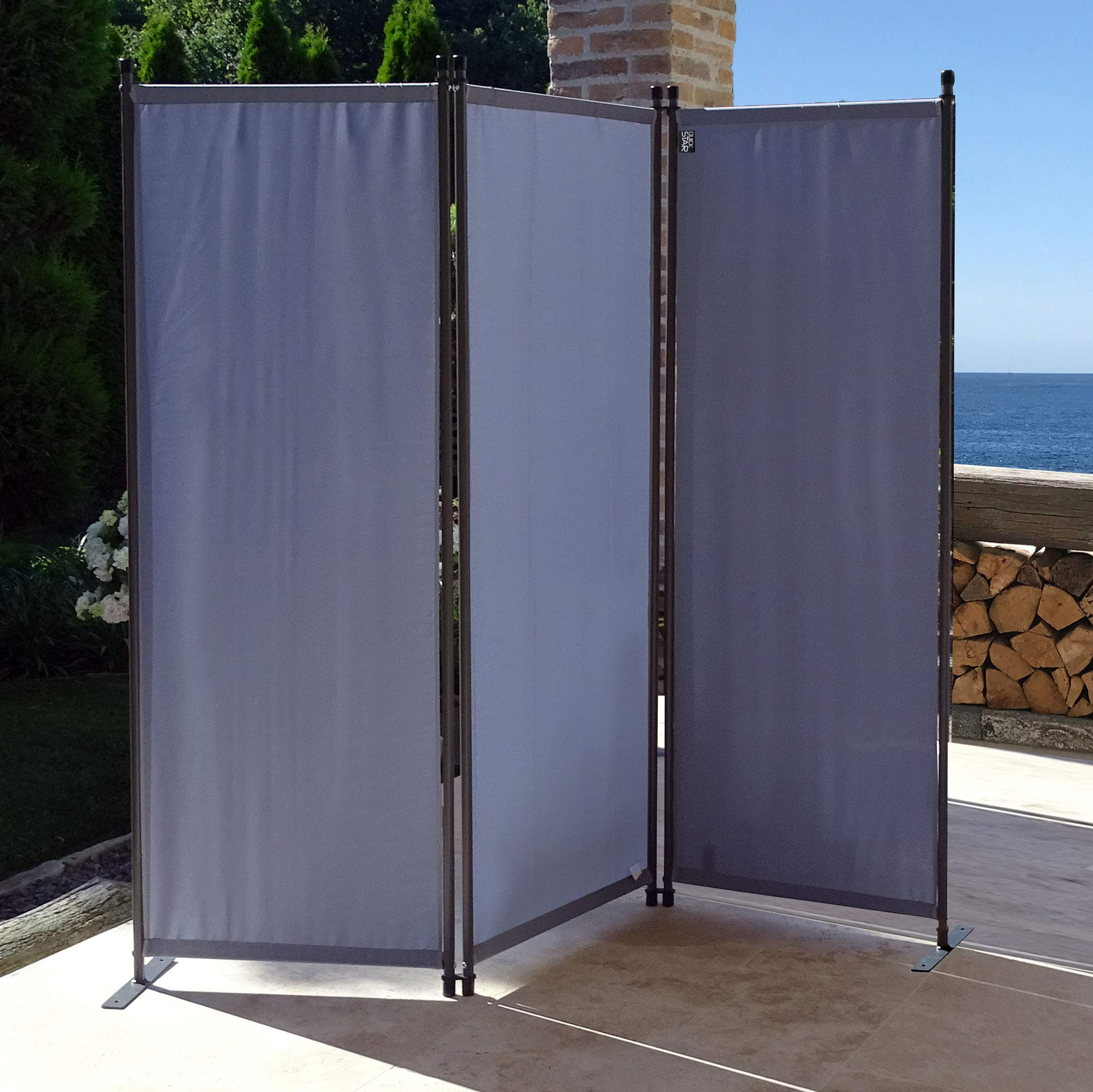 Ein grauer dreiteiliger Paravent steht draußen auf einer Terrasse vor dem Meer.