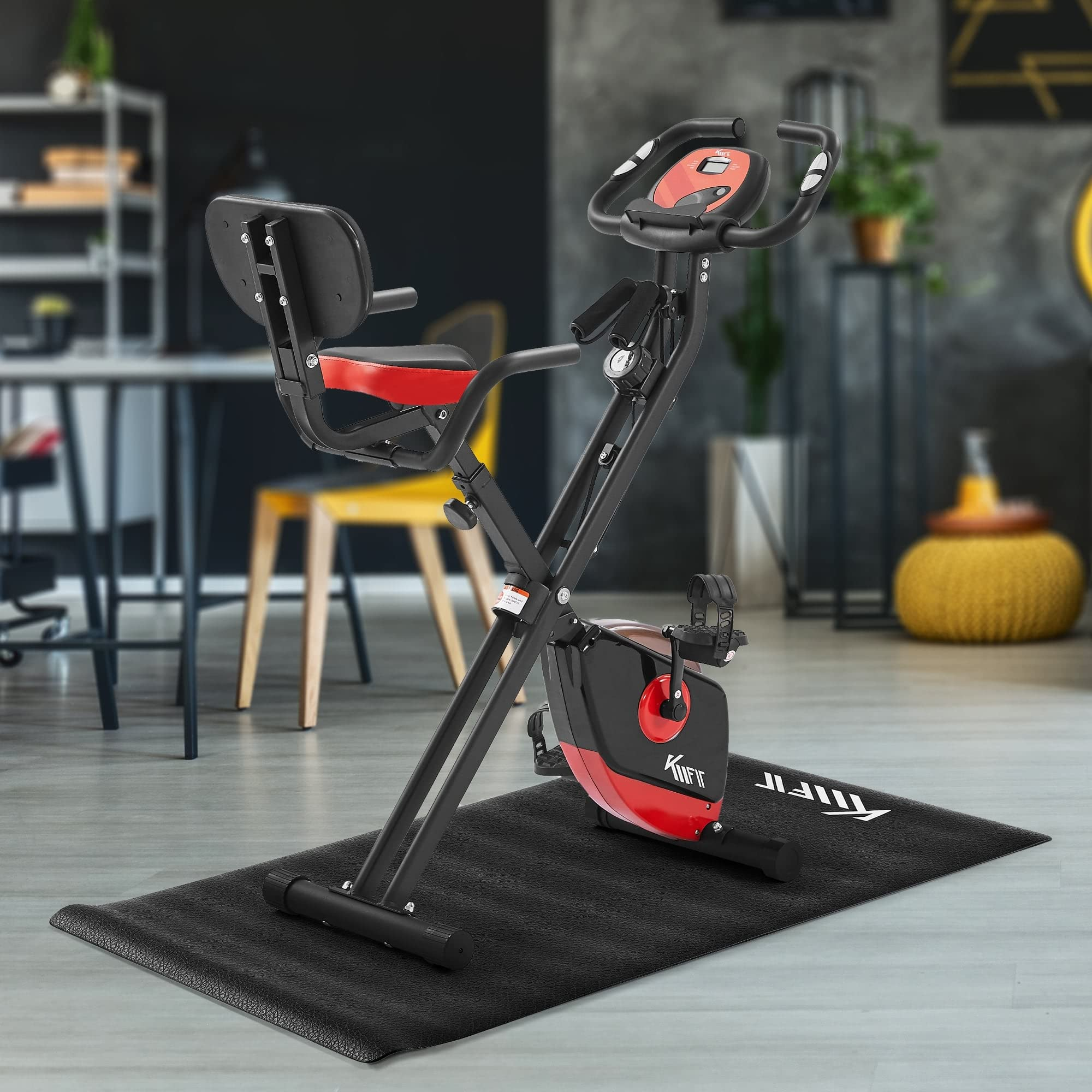 Ein schwarz-rotes Heimtrainer mit Rückenlehne steht auf einer schwarzen Matte in einem Raum.