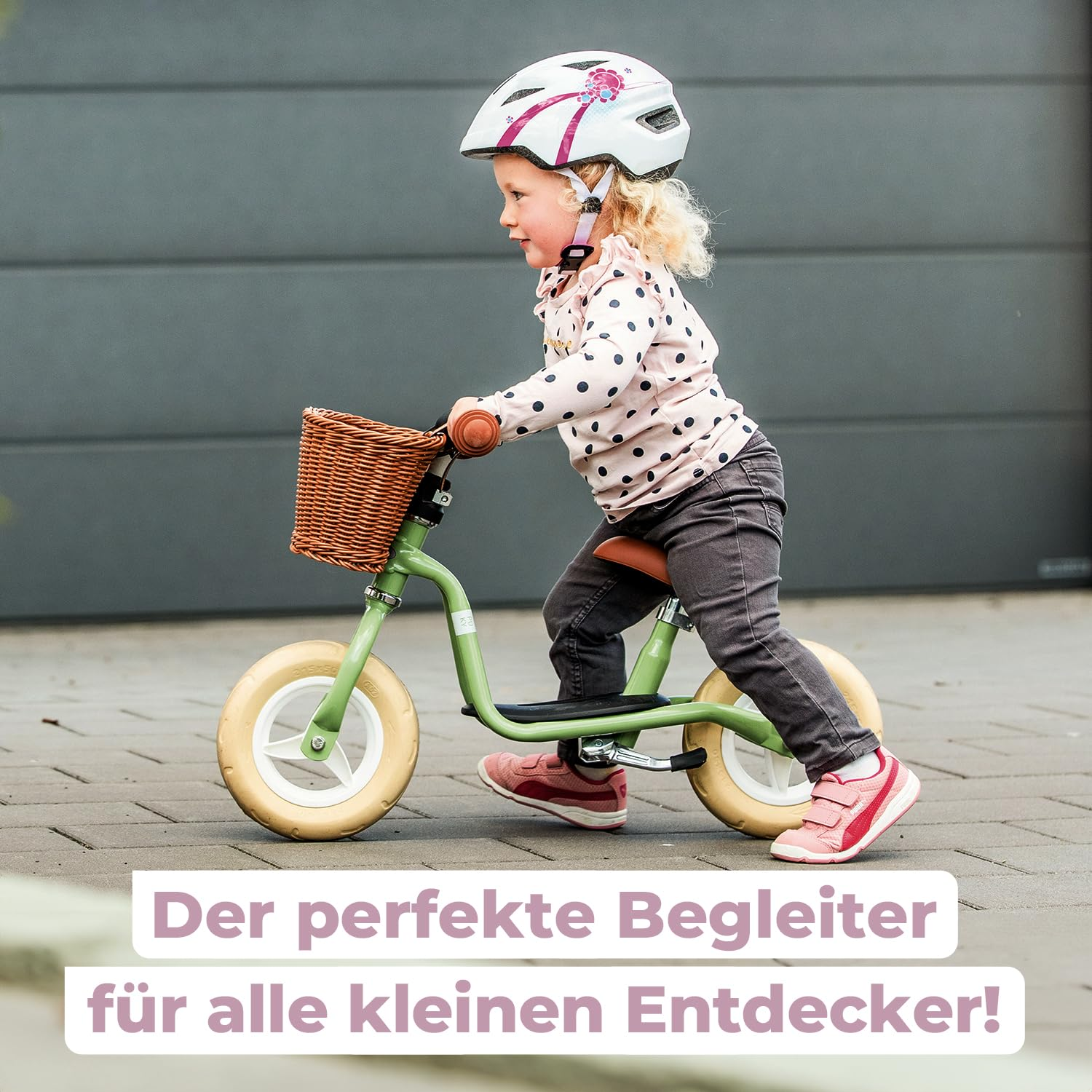 Un tout-petit avec un casque fait du vélo d'équilibre vert avec un panier.