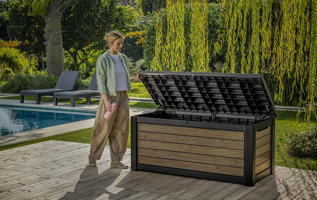 Eine Frau öffnet eine holzfarbene Aufbewahrungsbox auf einer Holzterrasse am Pool.