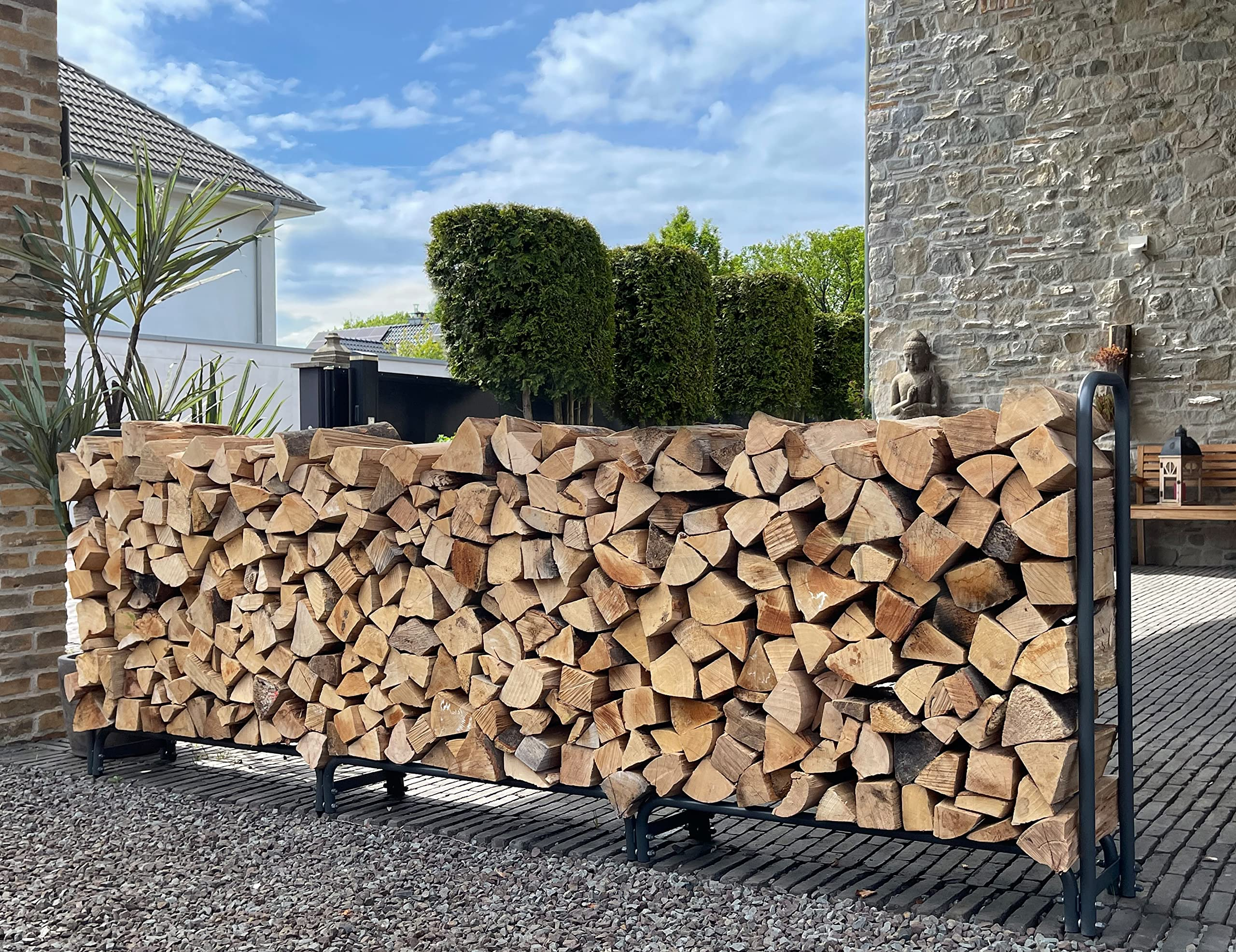 Une pile de bois de chauffage soigneusement rangée dans un support en métal, devant un mur en pierre.