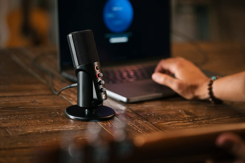 Un microfono nero si trova su una scrivania di legno davanti a un computer portatile.