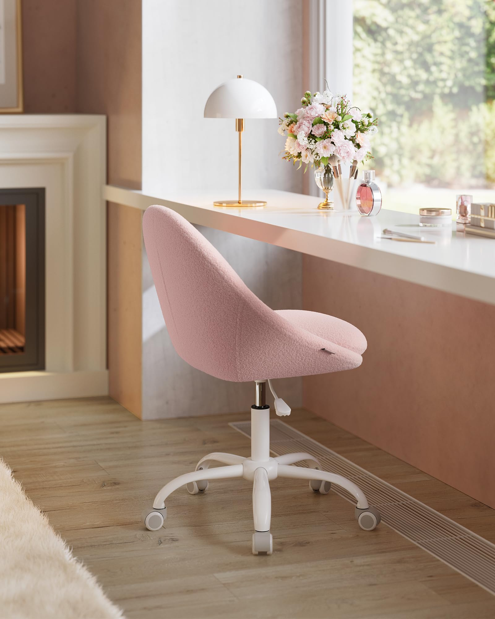 Une chaise rose à roulettes est devant un bureau blanc avec une lampe et des fleurs.