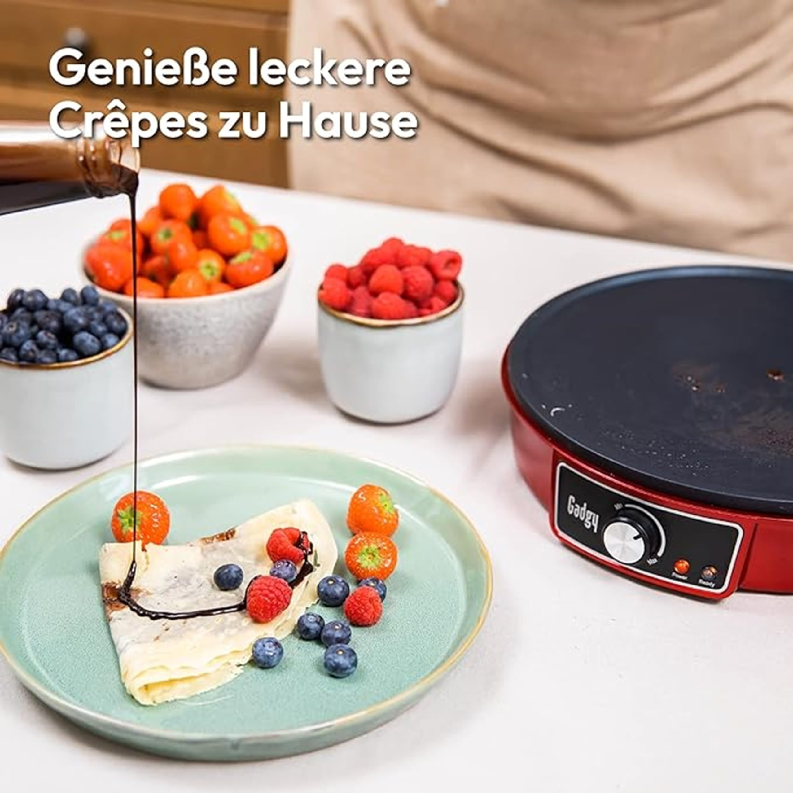 Une crêpe sur une assiette verte avec des baies et du chocolat, et une crêpière rouge.