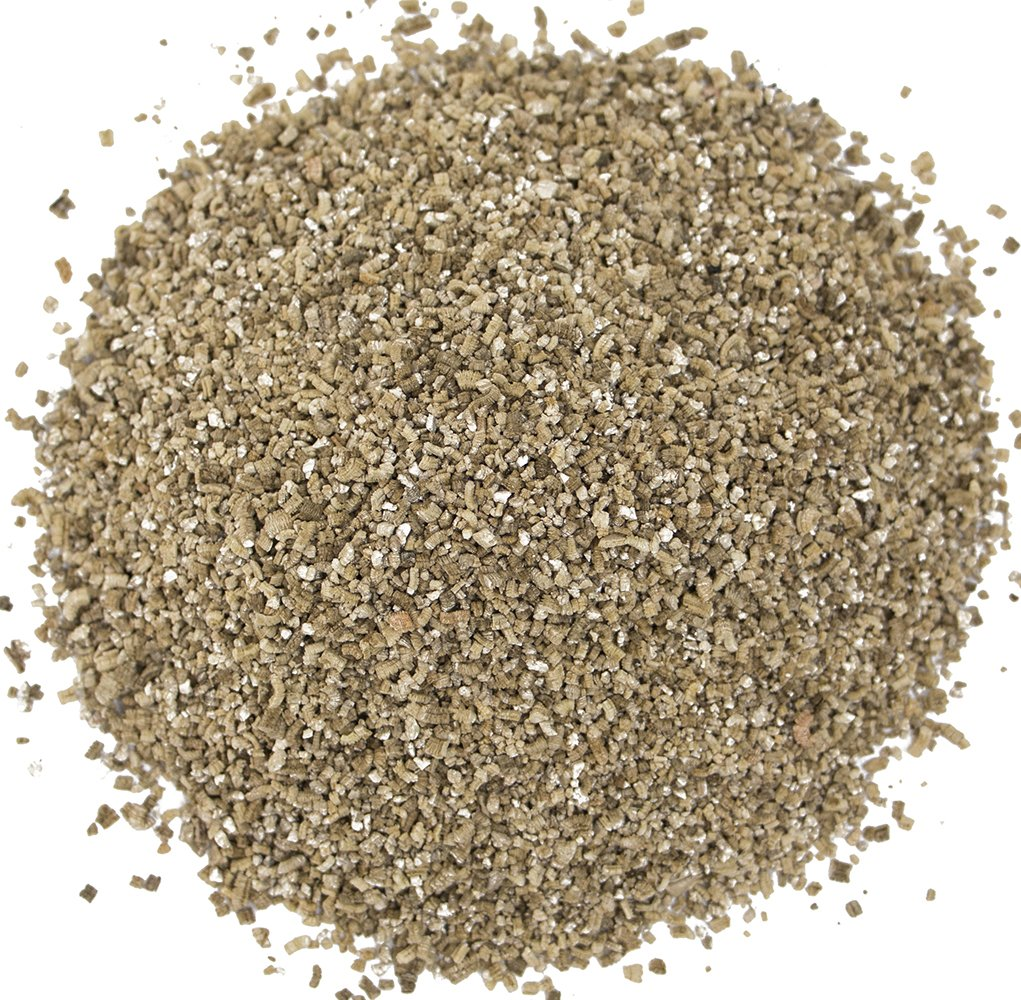 Gros plan de granules grossiers, brunâtres et grisâtres sur fond blanc.