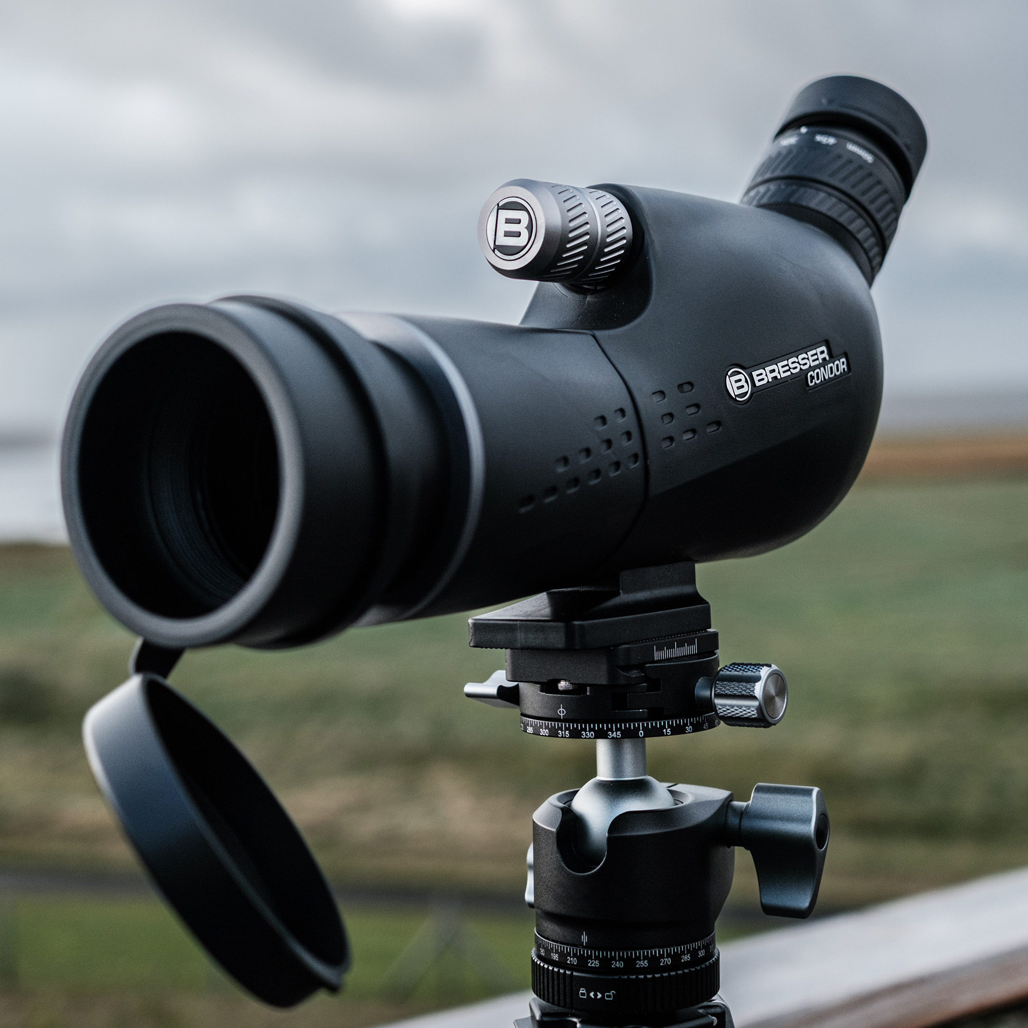 Un telescopio terrestre Bresser negro montado en un trípode con un paisaje de fondo.