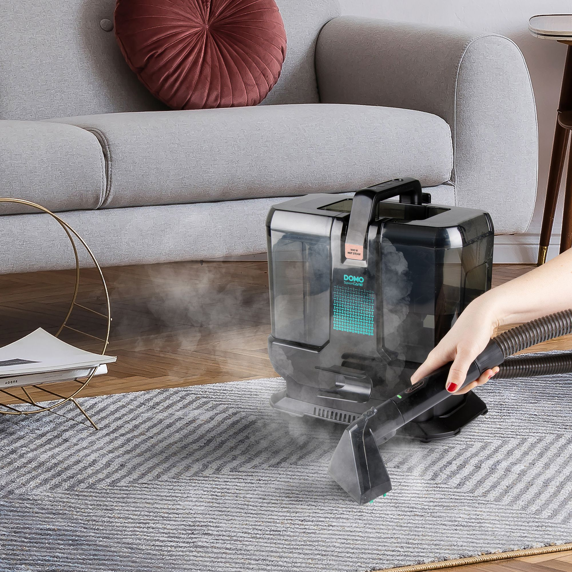 Ein Handreiniger saugt Dampf auf einem grauen Teppich vor einem Sofa.