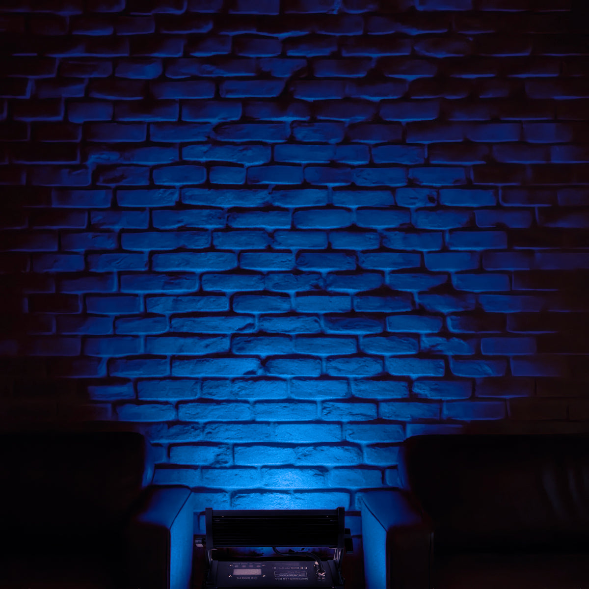 Eine Backsteinwand wird von unten blau beleuchtet, flankiert von zwei Sesseln.