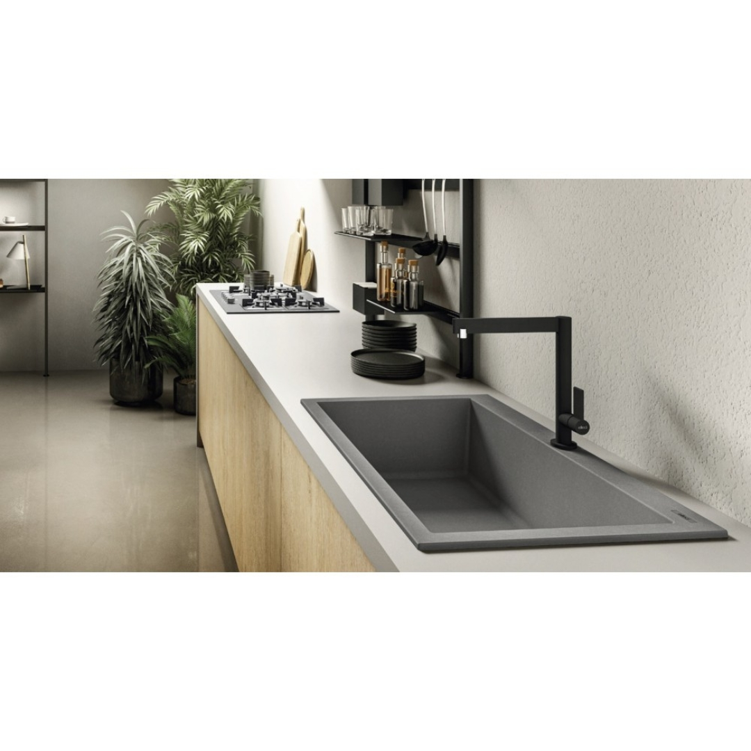 Cucina moderna con piano grigio, lavello scuro, rubinetto nero, mobili in legno e piante in vaso sullo sfondo.