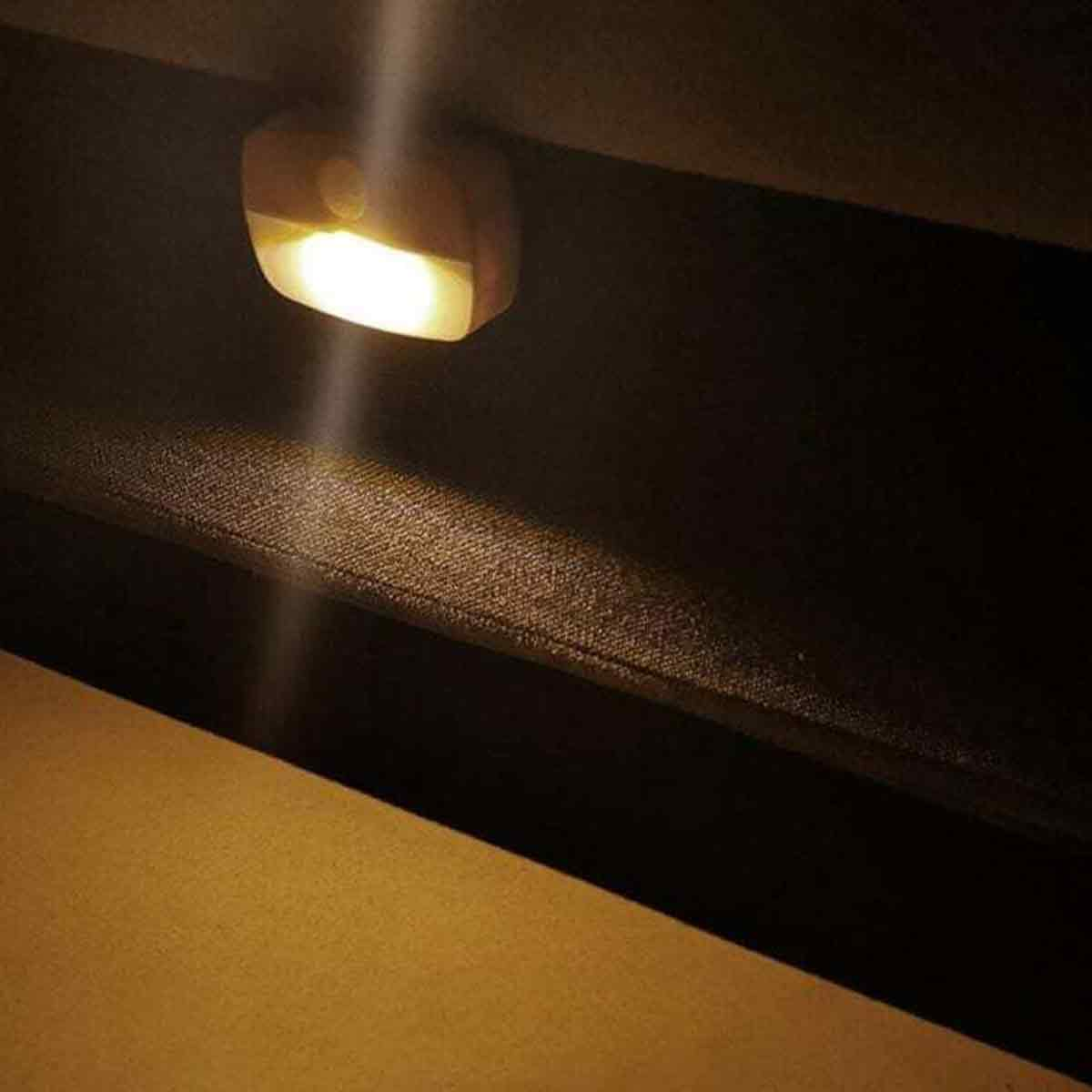 Eine kleine weiße LED-Sensorleuchte an einer dunklen Oberfläche wirft ein warmes Licht auf einen Holzvorsprung.