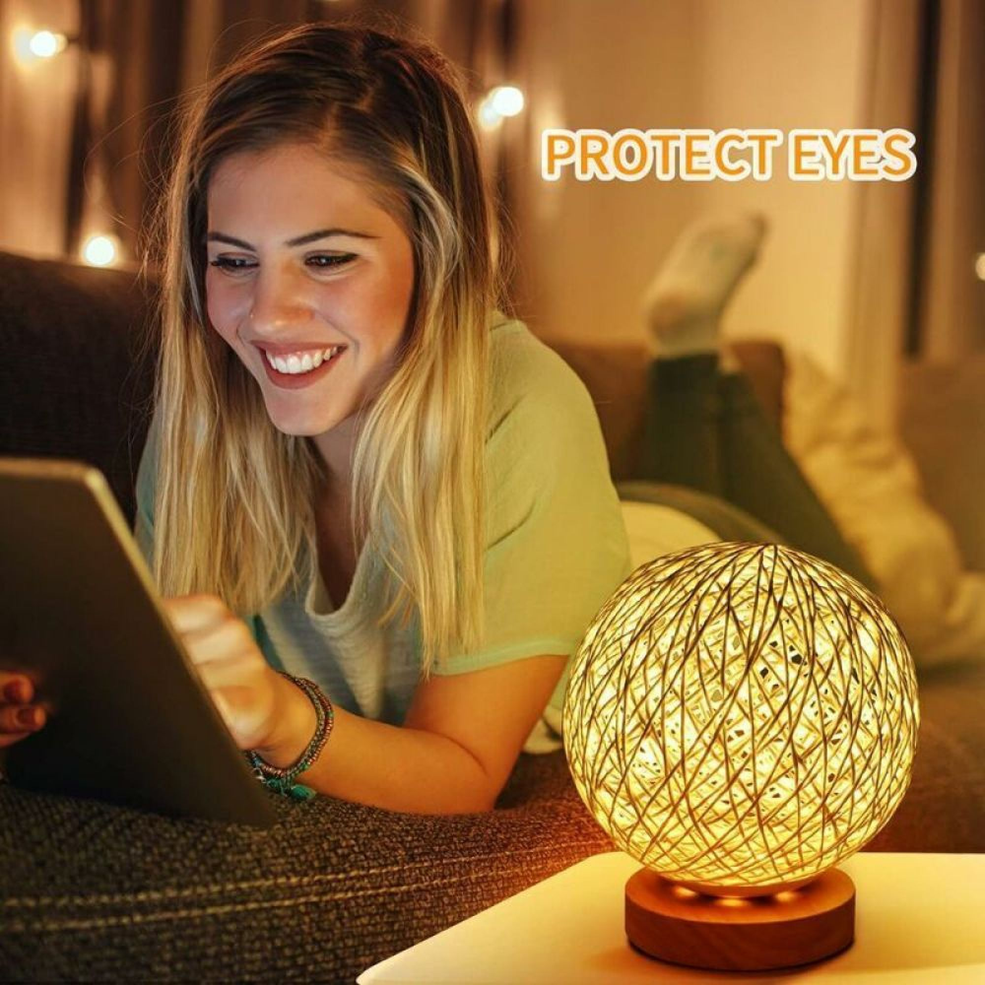 Eine blonde Frau lächelt und nutzt ein Tablet auf einer Couch, neben einer runden Lampe.
