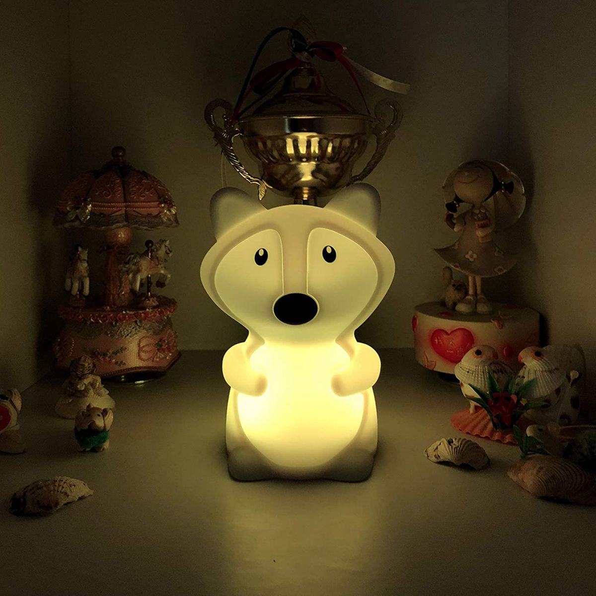 Eine leuchtende, fuchsähnliche Nachtlampe steht auf einem Regal vor verschiedenen Dekorationsobjekten.