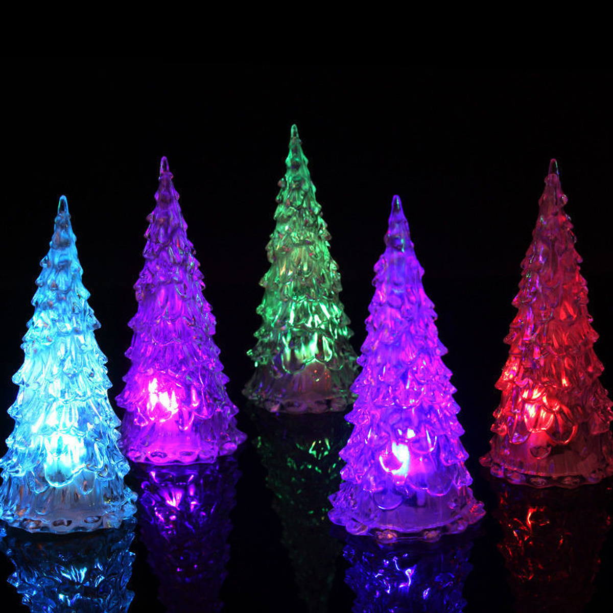 Fünf leuchtende, bunte Christbaumfiguren aus Plastik vor schwarzem Hintergrund, die sich auf einer dunklen Fläche spiegeln.