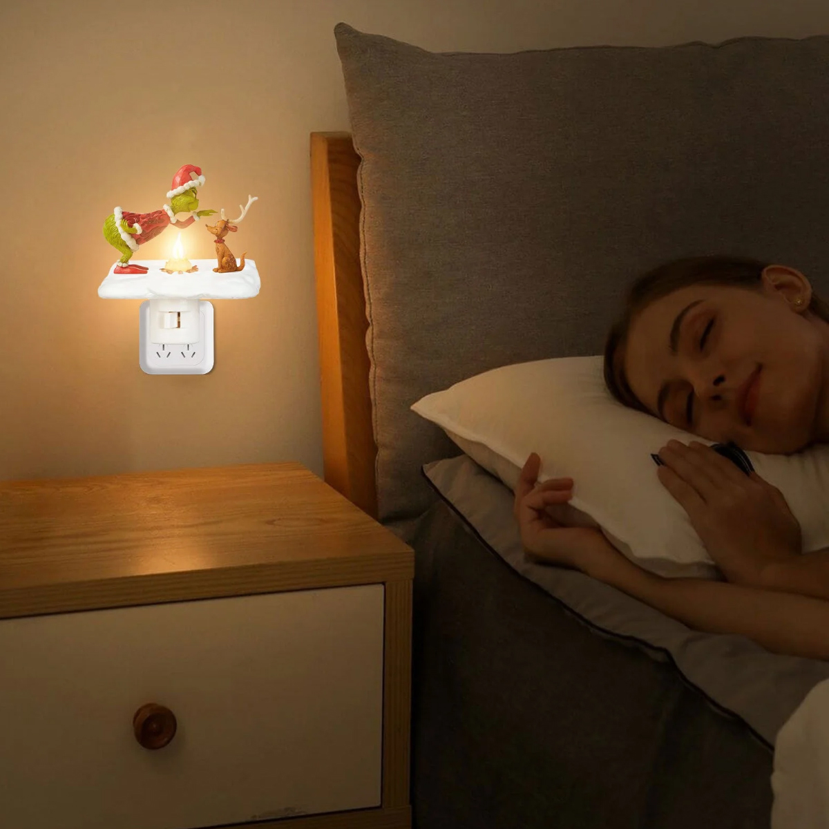Eine Frau schläft im Bett neben einem Nachttisch mit einer leuchtenden Grinch-Nachtlampe an der Wand.