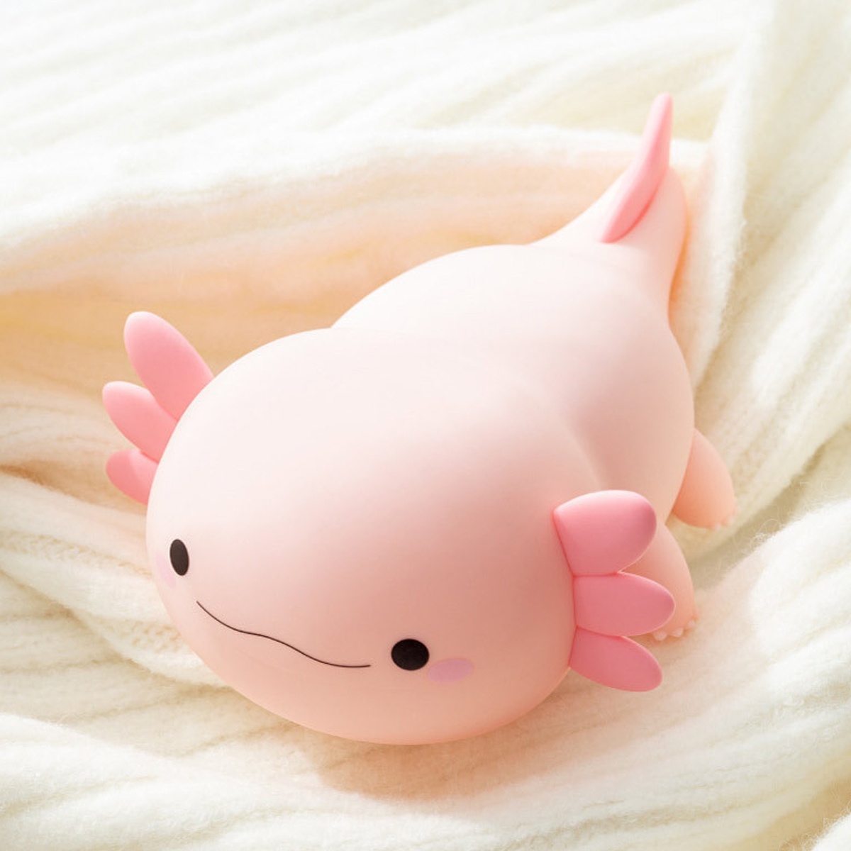 Ein süßes, rosafarbenes Axolotl-Nachtlicht ruht auf einer weichen, weißen Decke.