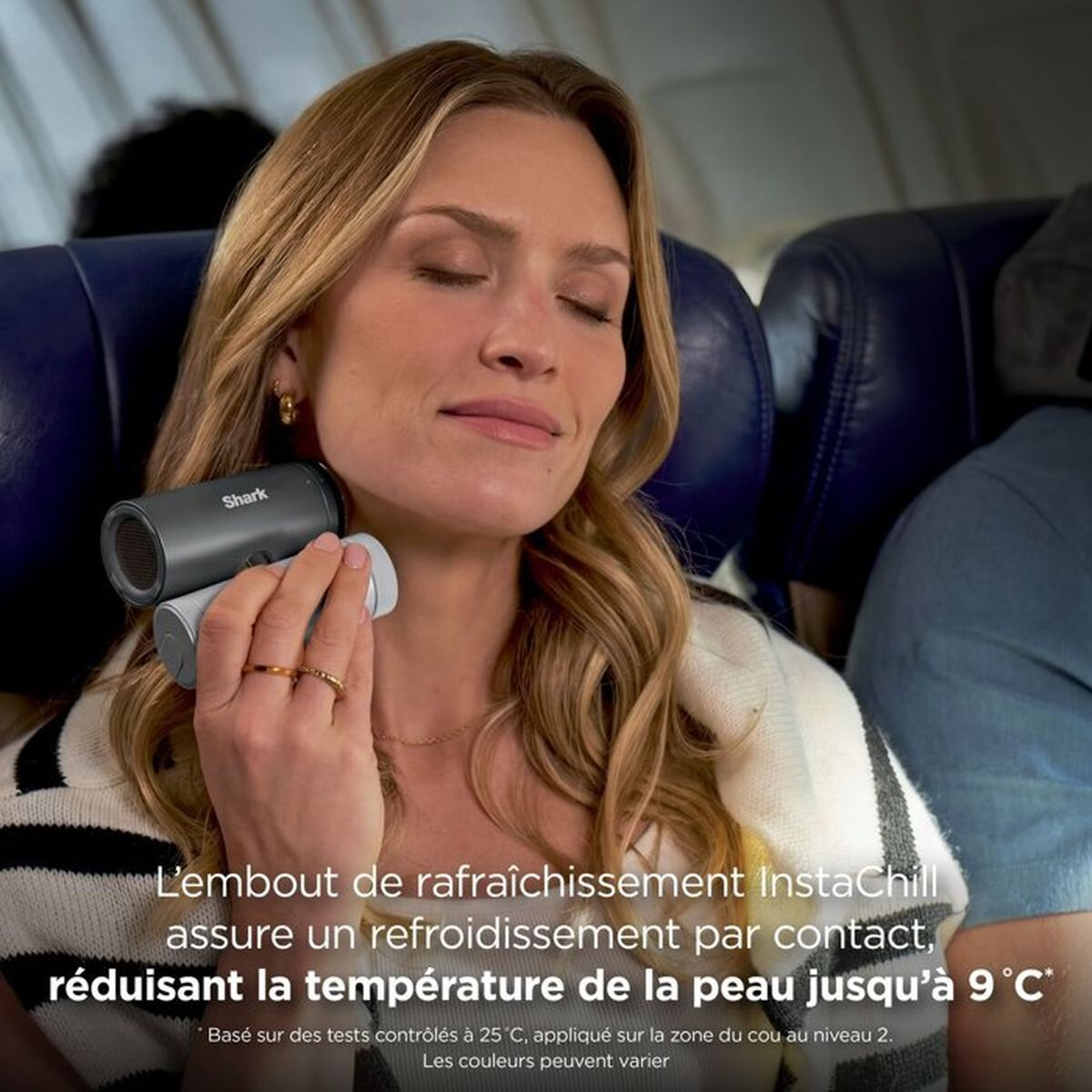 Una donna bionda tiene un dispositivo Shark InstaChill sul collo per rinfrescarsi in aereo.