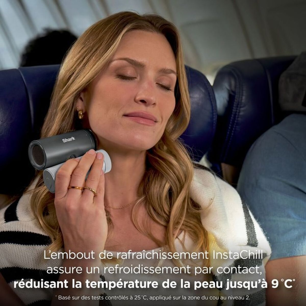 Una donna bionda tiene un dispositivo Shark grigio sul collo, sorridendo con gli occhi chiusi in aereo.