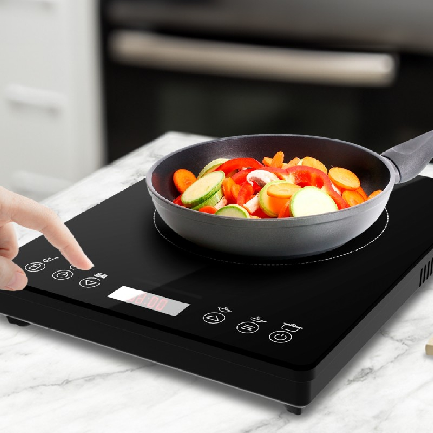 Mano presionando el panel de control de una placa de inducción con verduras.