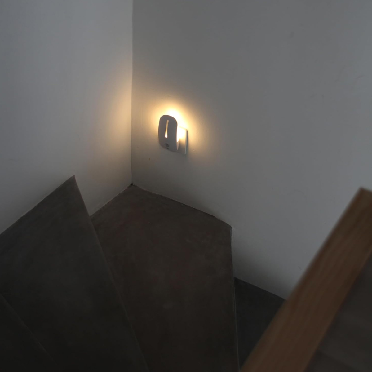 Eine kleine weiße LED-Treppenleuchte leuchtet an einer Wand in einer dunklen Treppe.