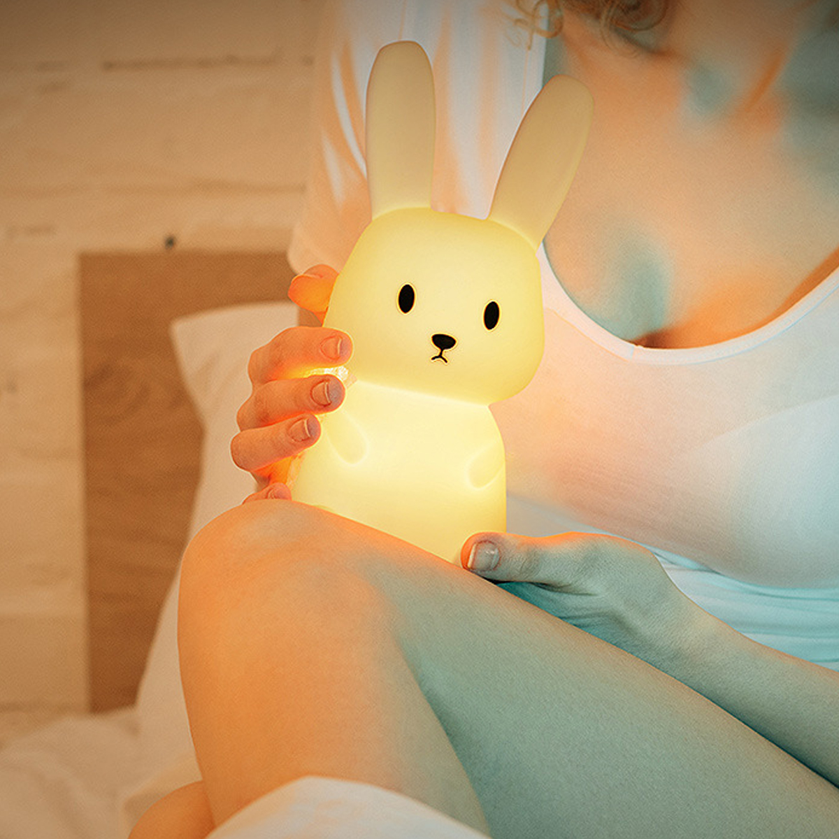 Eine Person hält ein leuchtendes, gelbes, hasenförmiges Nachtlicht in einem schlafzimmer.