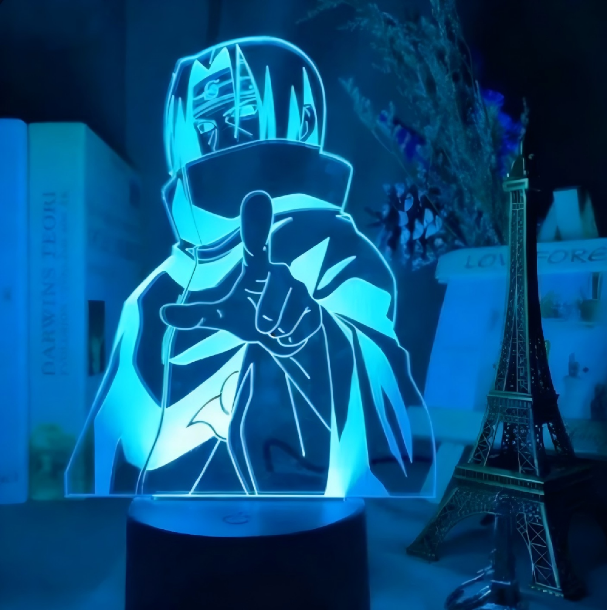 Eine blau leuchtende 3D-Anime-Lampe zeigt Itachi Uchiha mit erhobenem Finger vor einem Eiffelturm-Modell.