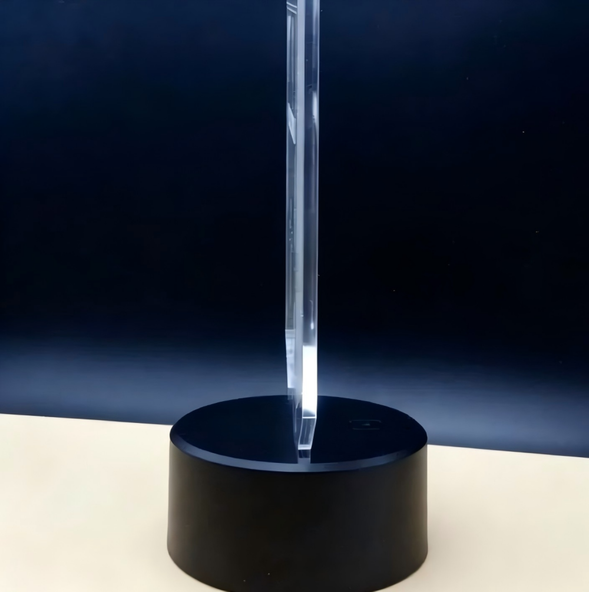 Eine durchsichtige Acrylplatte steht auf einem runden, schwarzen Sockel vor einem dunklen Hintergrund.