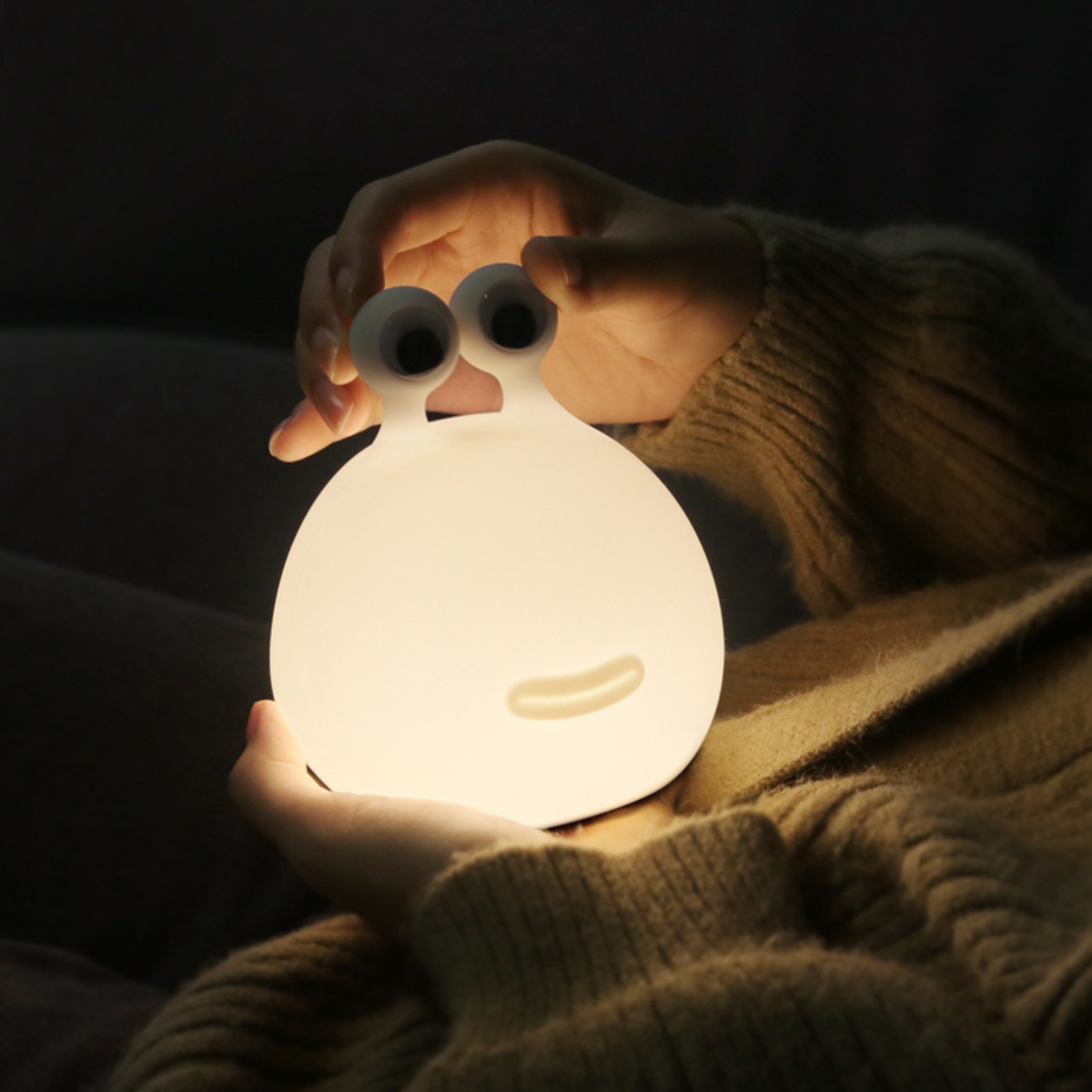 Eine Person hält eine weiße, leuchtende Schneckenlampe mit großen Augen in den Händen.