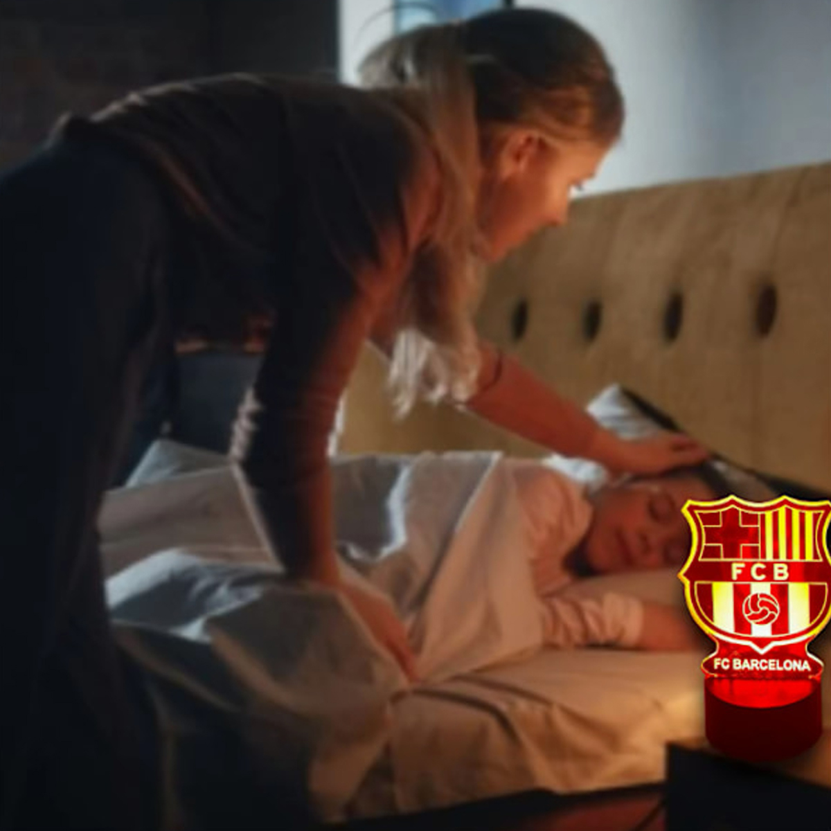 Eine Frau deckt ein Kind im Bett zu, daneben leuchtet eine FC-Barcelona-Lampe.