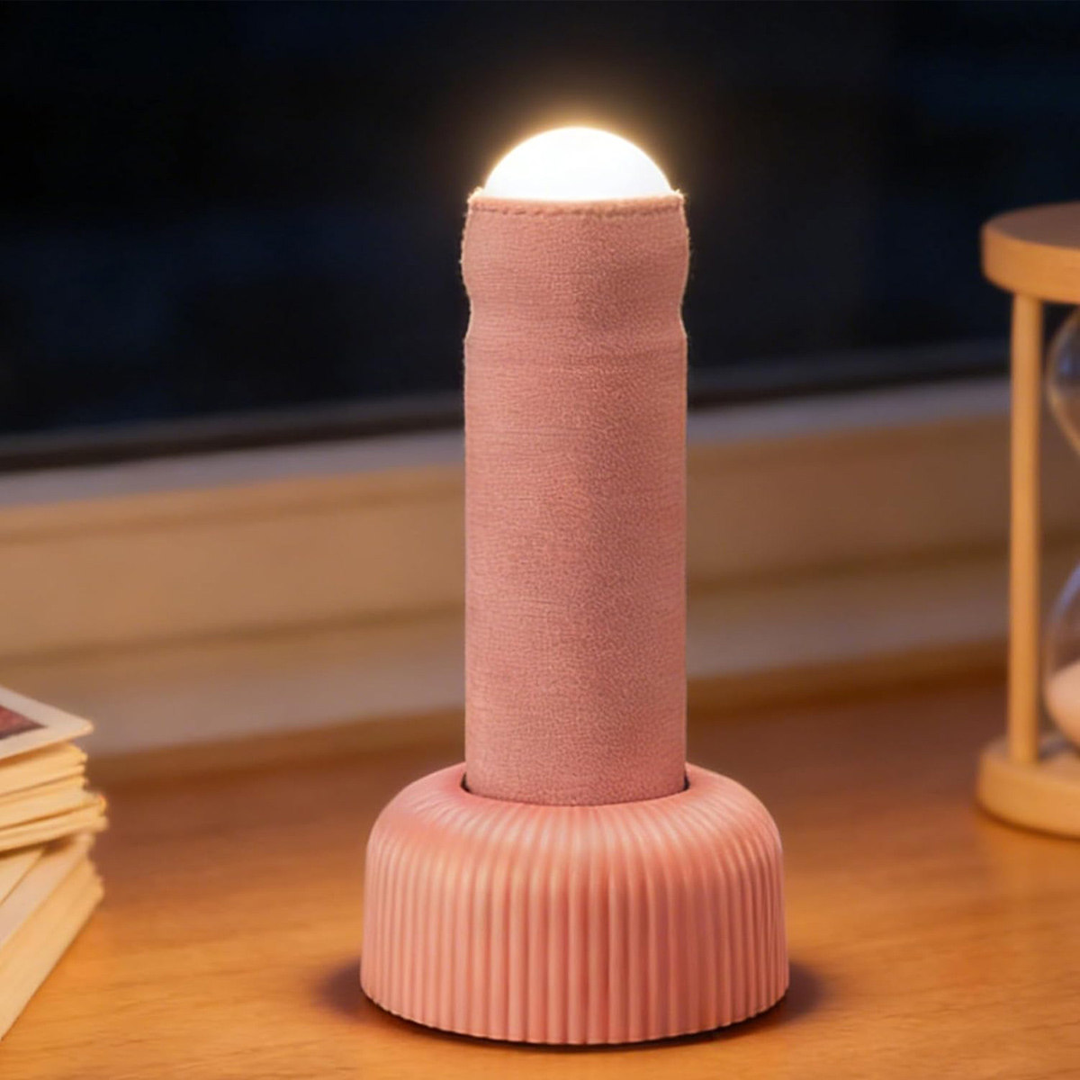Ein rosafarbenes, stoffbezogenes Nachtlicht steht auf einem Holztisch mit einer glühenden Glühbirne oben.