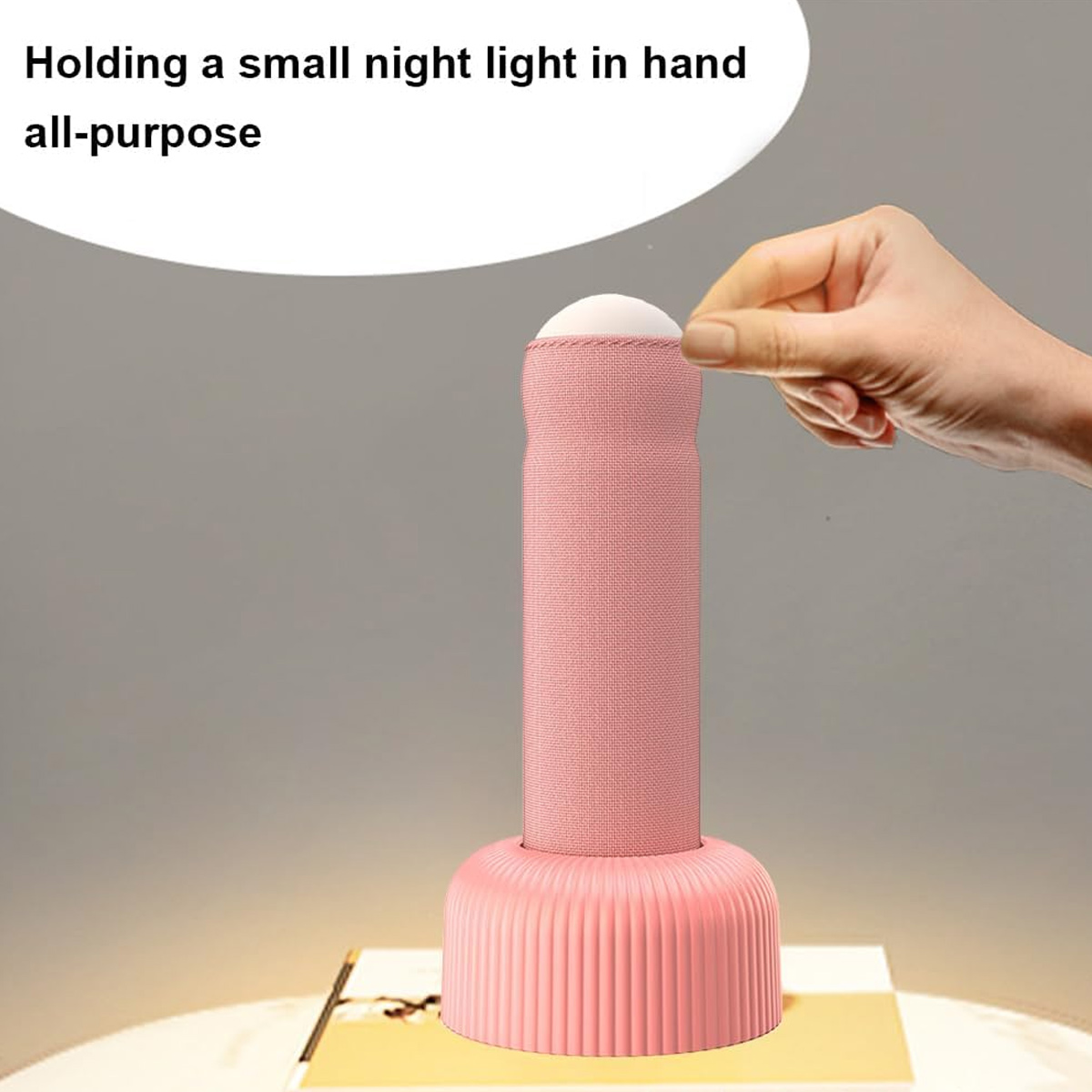 Eine Hand schaltet eine rosa, zylindrische Nachtlampe ein, die auf einer weißen Basis vor grauem Hintergrund steht.