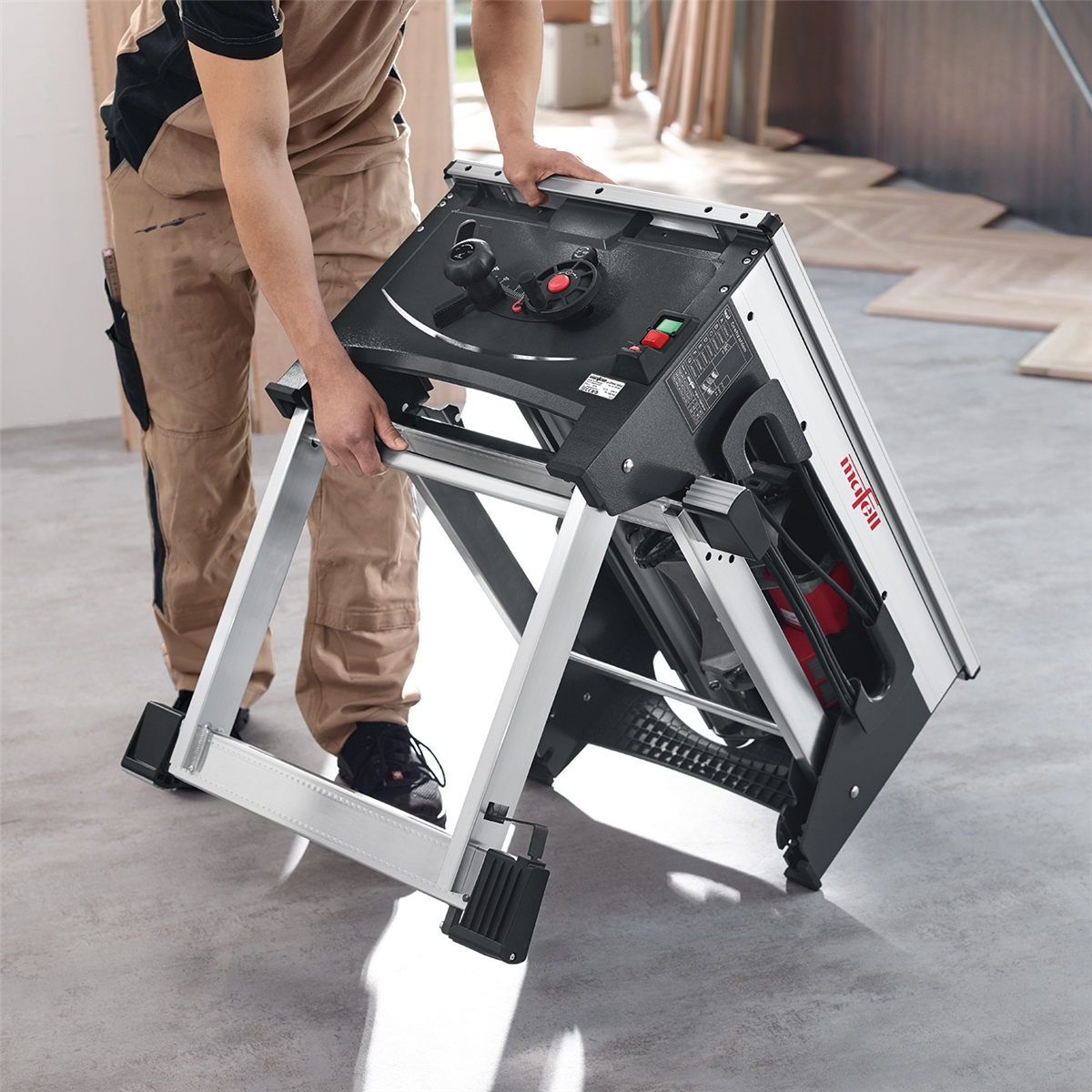 Ein Handwerker faltet eine Mafell Tischkreissäge auf einem hellen Betonboden zusammen.