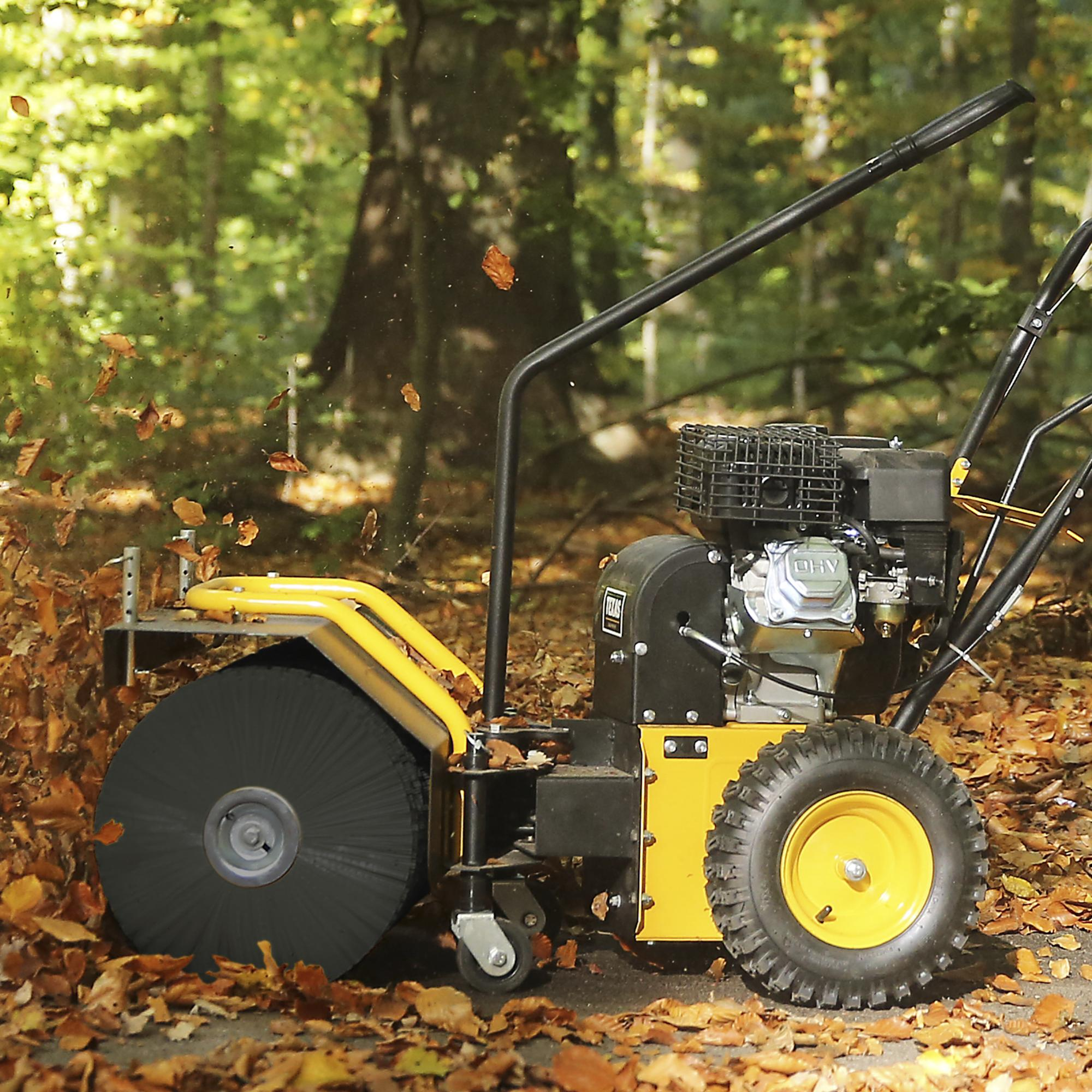 Eine gelb-schwarze Motor-Kehrmaschine räumt Herbstlaub in einem Wald.