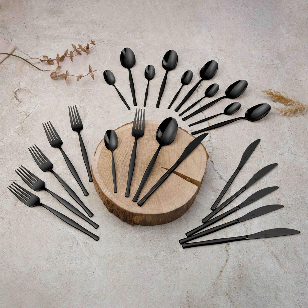 Un ensemble de couverts noir mat disposés sur un fond en pierre avec un bloc de bois.